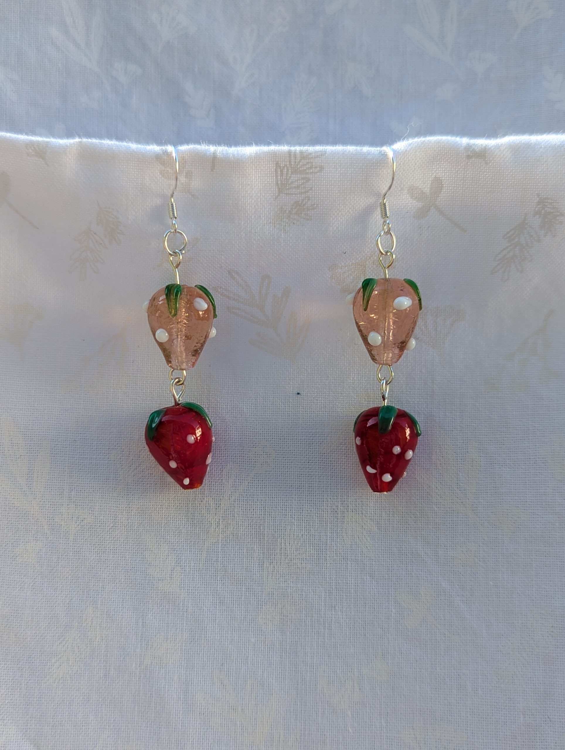 Handmade glass strawberry patch earrings with red, pale pink, green, and white details on sterling silver hooks.