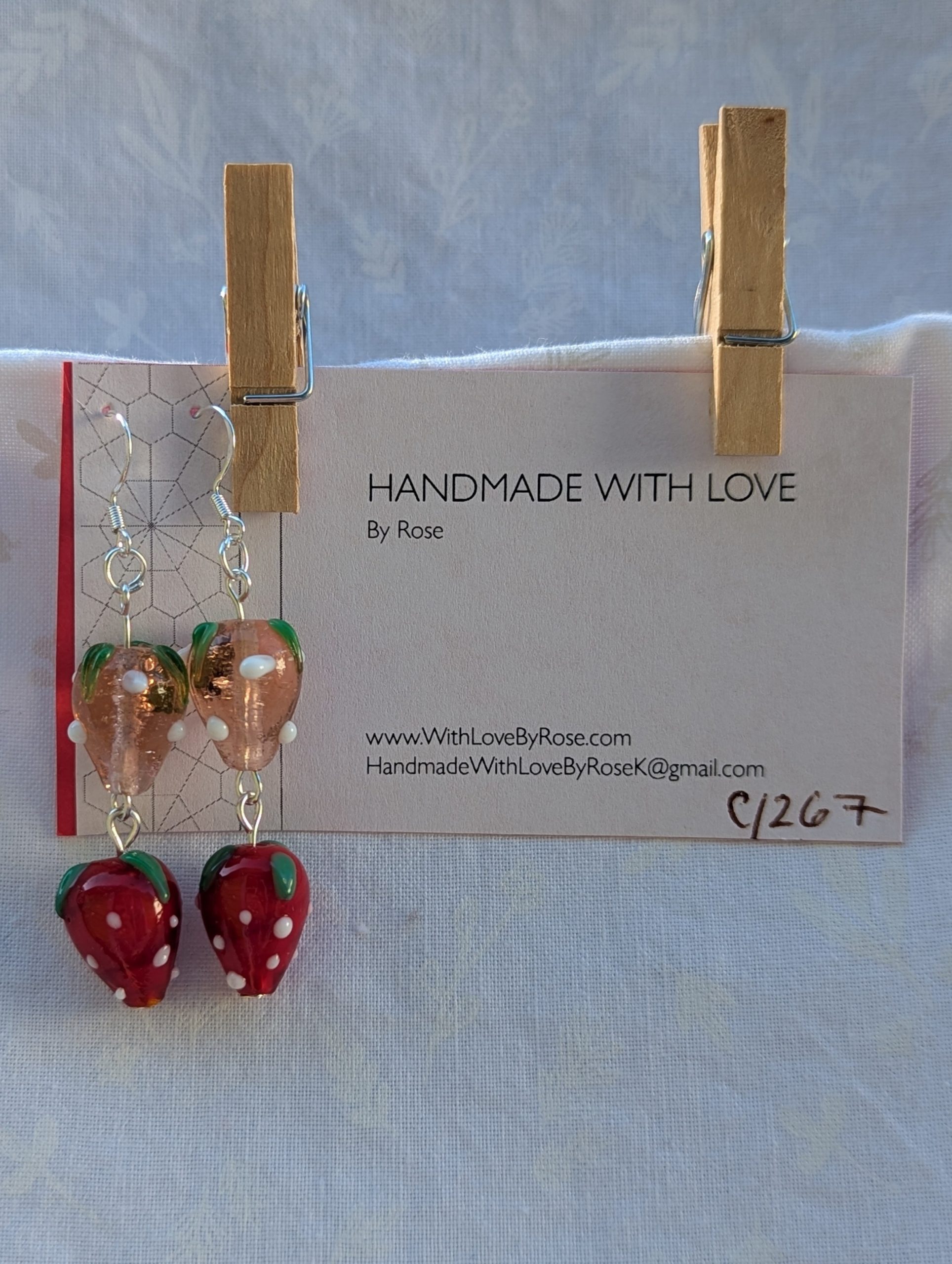 Handmade glass strawberry patch earrings with red, pale pink, green, and white details on sterling silver hooks.