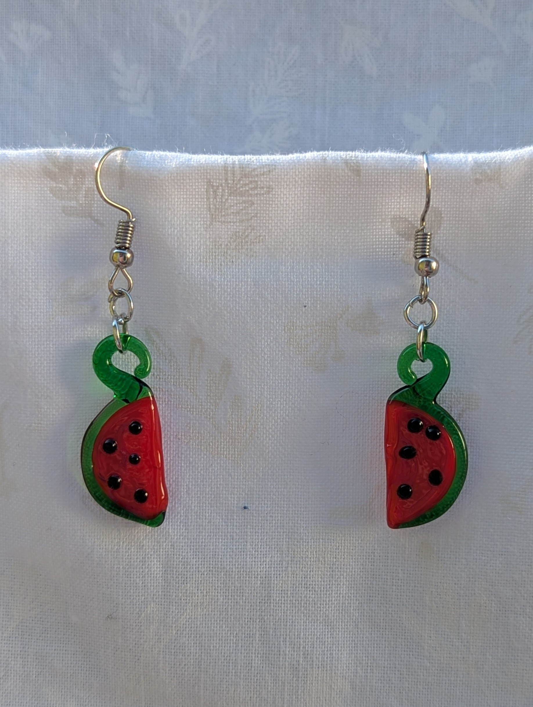 Handmade glass watermelon slice earrings with pink-red centers, green rinds, and sterling silver hooks.