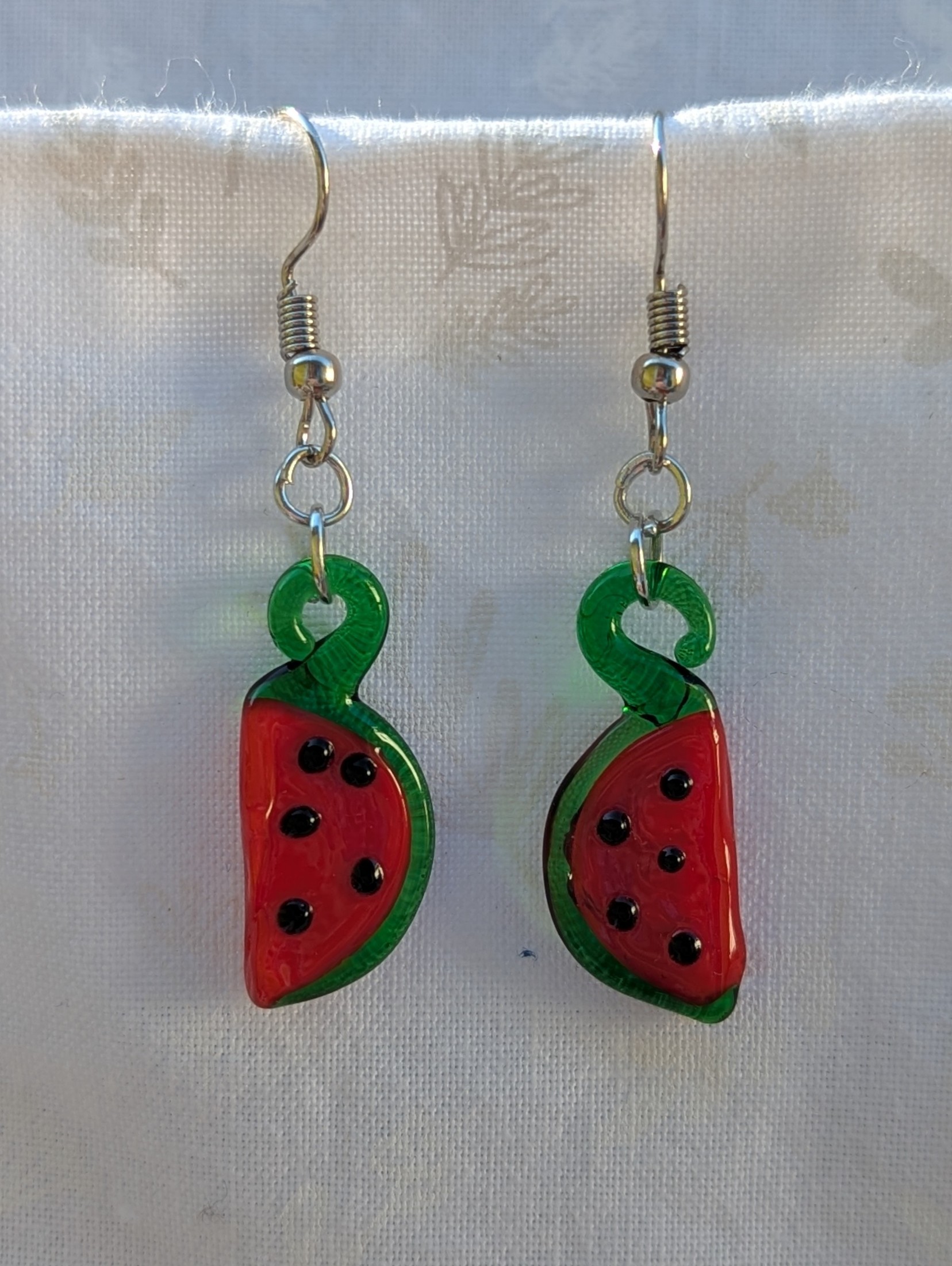 Handmade glass watermelon slice earrings with pink-red centers, green rinds, and sterling silver hooks.