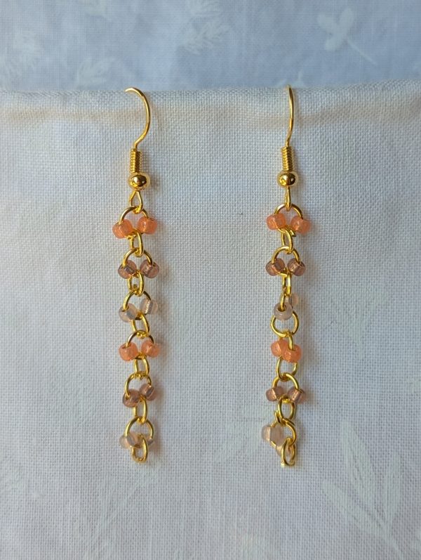 Handmade gold beaded earrings with 12 peach and champagne glass beads connected by gold-colored metal and matching hooks.