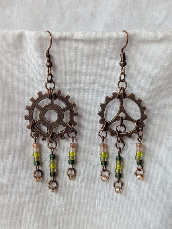 Handmade bronze gear steampunk earrings with green and brown glass beads, asymmetrical steampunk design, and antique bronze hooks.