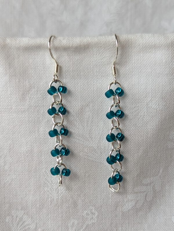 Handmade teal glass earrings featuring frosted and silver-lined teal beads connected with silver jump rings and sterling silver hooks.