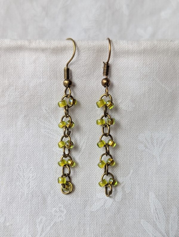 Handmade green glass earrings featuring fluorescent and iridescent green beads connected with bronze jump rings and hooks.