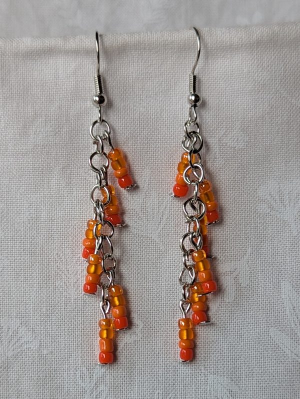 Sunset Ember: Handmade orange beaded earrings featuring four shades of glass beads—tangerine, coral, amber, and peach—linked with steel-colored jump rings and hooks.