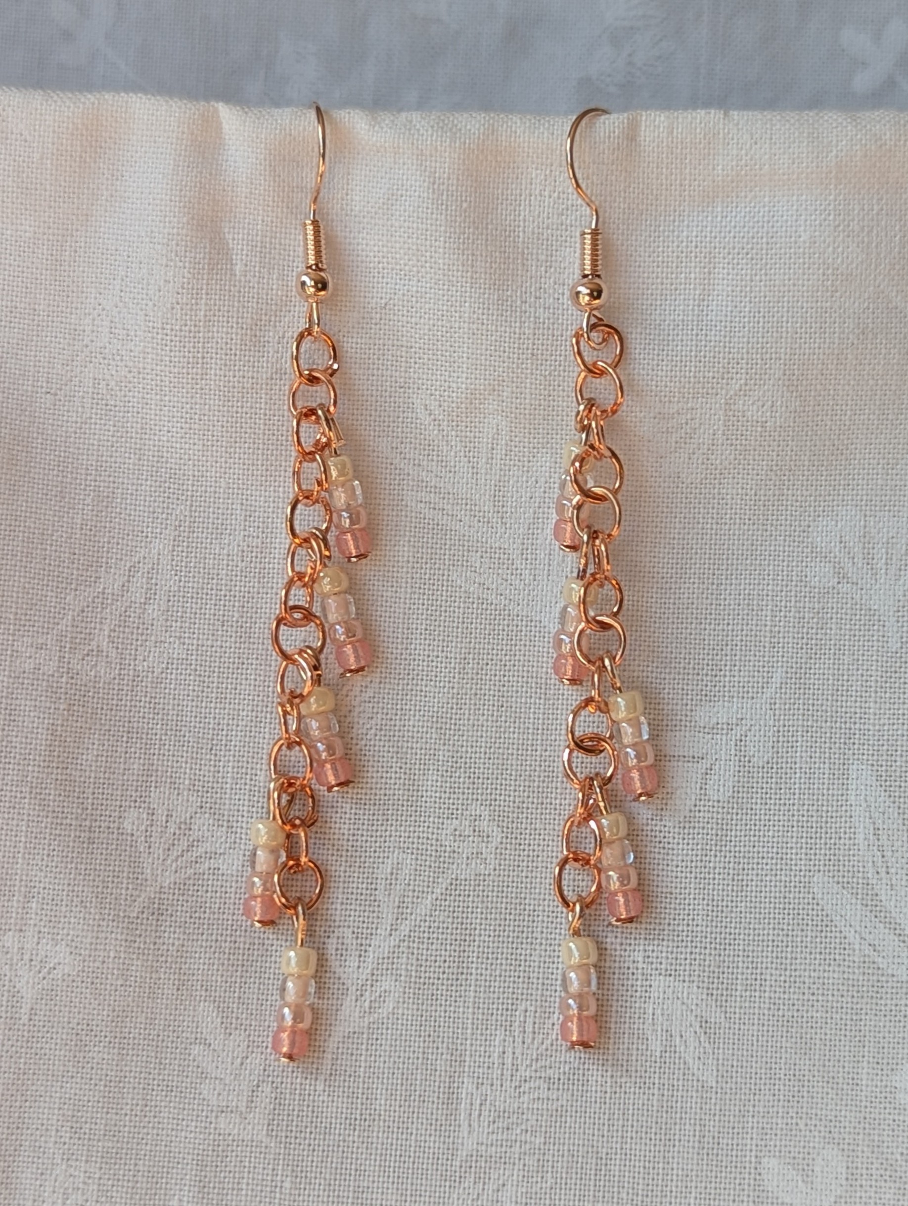 Handmade blush cream beaded earrings featuring pale pink and cream glass beads in four shades, linked with copper jump rings and rose-gold hooks.