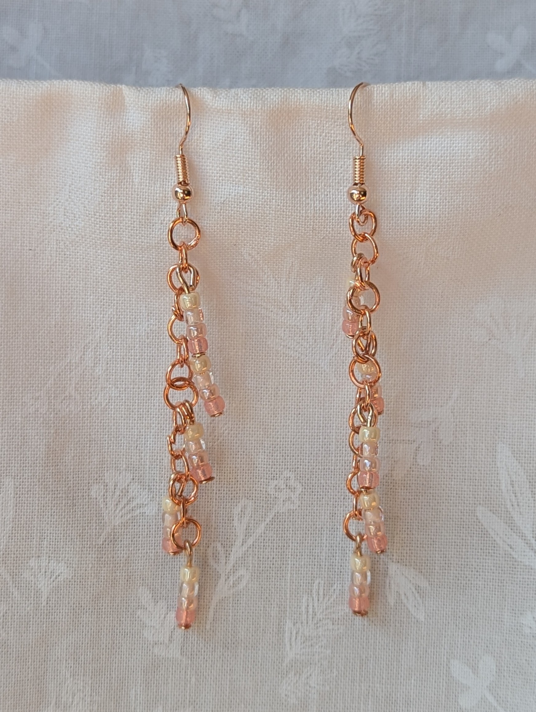 Handmade blush cream beaded earrings featuring pale pink and cream glass beads in four shades, linked with copper jump rings and rose-gold hooks.