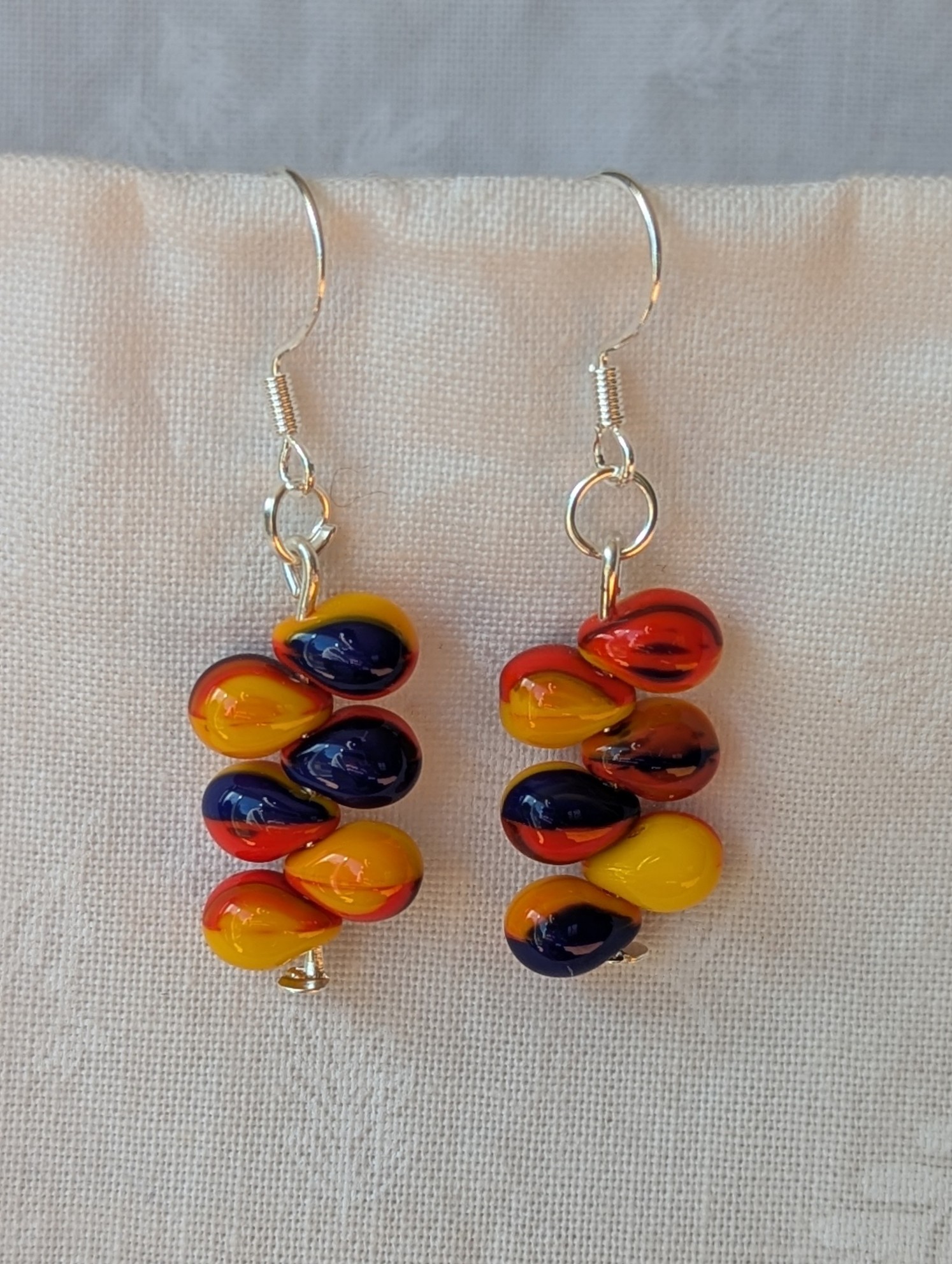 Handmade fireburst glass bead earrings featuring yellow, red, and blue teardrop beads on silver pins with sterling silver hooks.