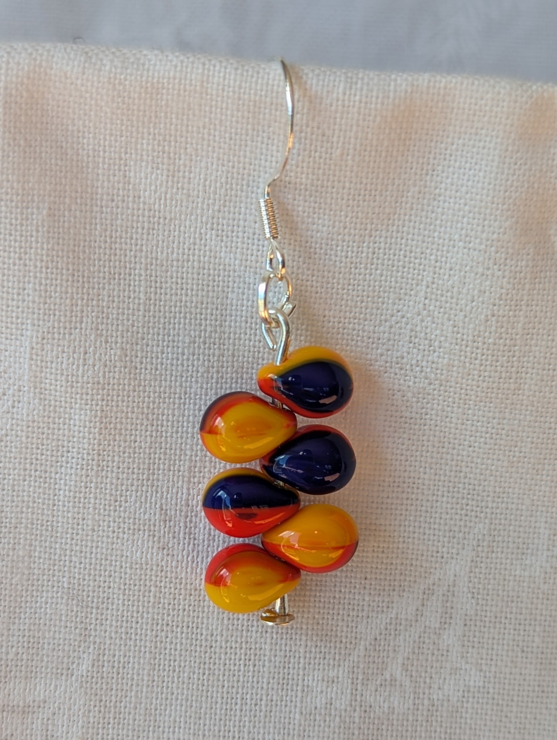 Handmade fireburst glass bead earrings featuring yellow, red, and blue teardrop beads on silver pins with sterling silver hooks.