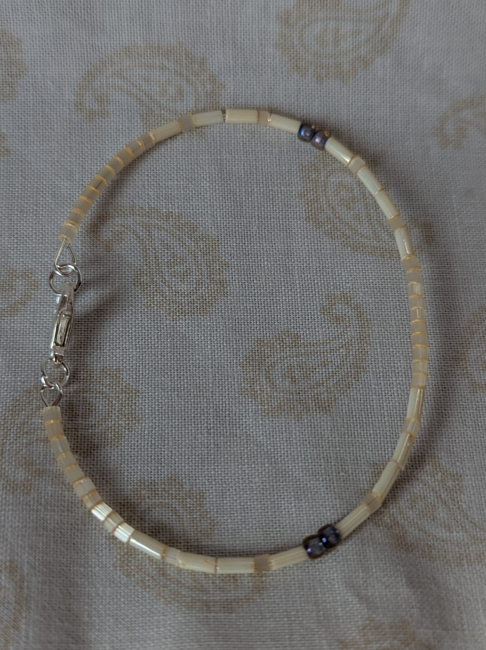 Handmade bracelet with short pearl-cream beads, long ivory-cream beads, and lavender-lined gray beads on silver-plated memory wire with a silver lobster clasp.