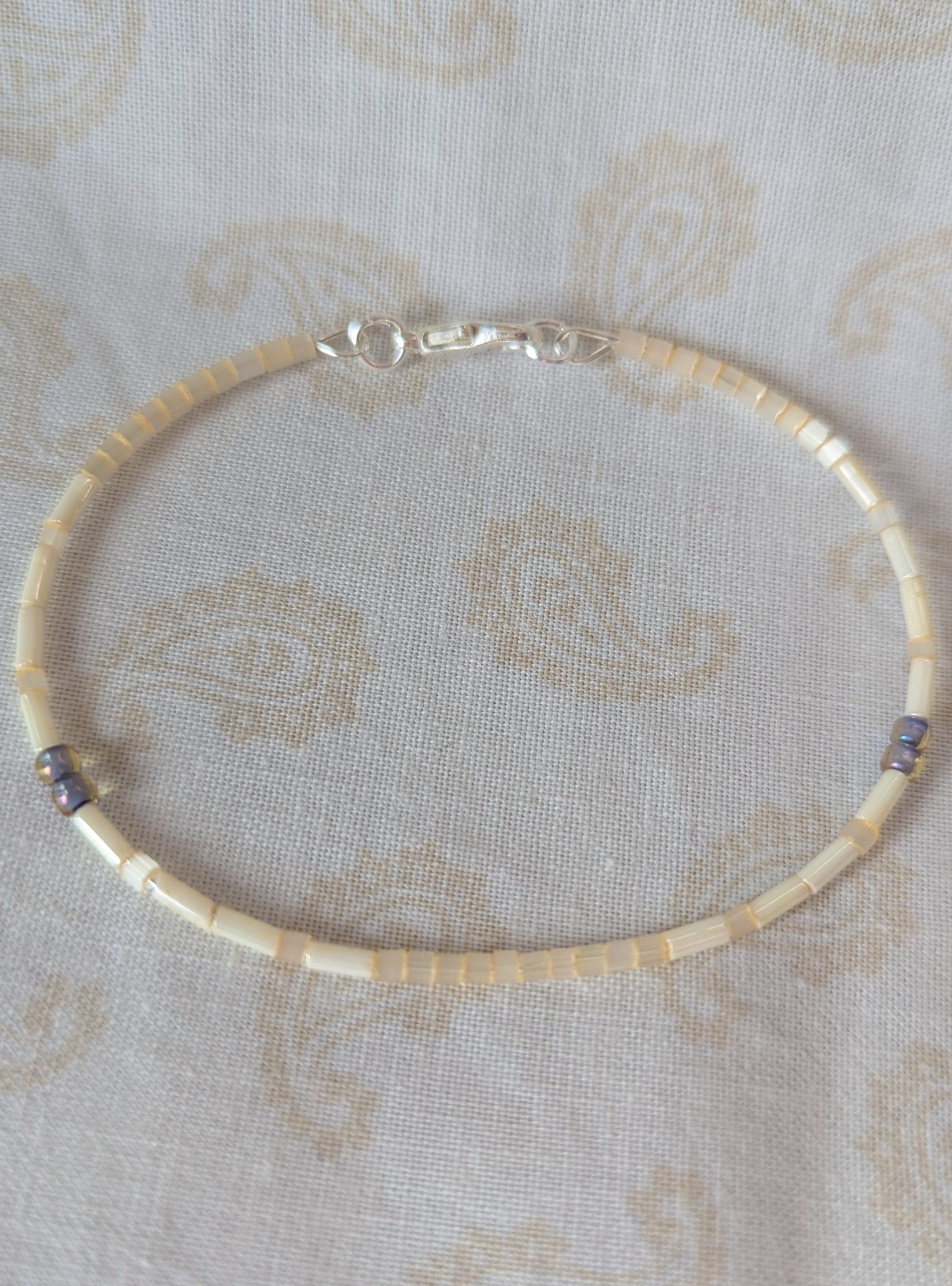 “Handmade bracelet with short pearl-cream beads, long ivory-cream beads, and lavender-lined gray beads on silver-plated memory wire with a silver lobster clasp.”