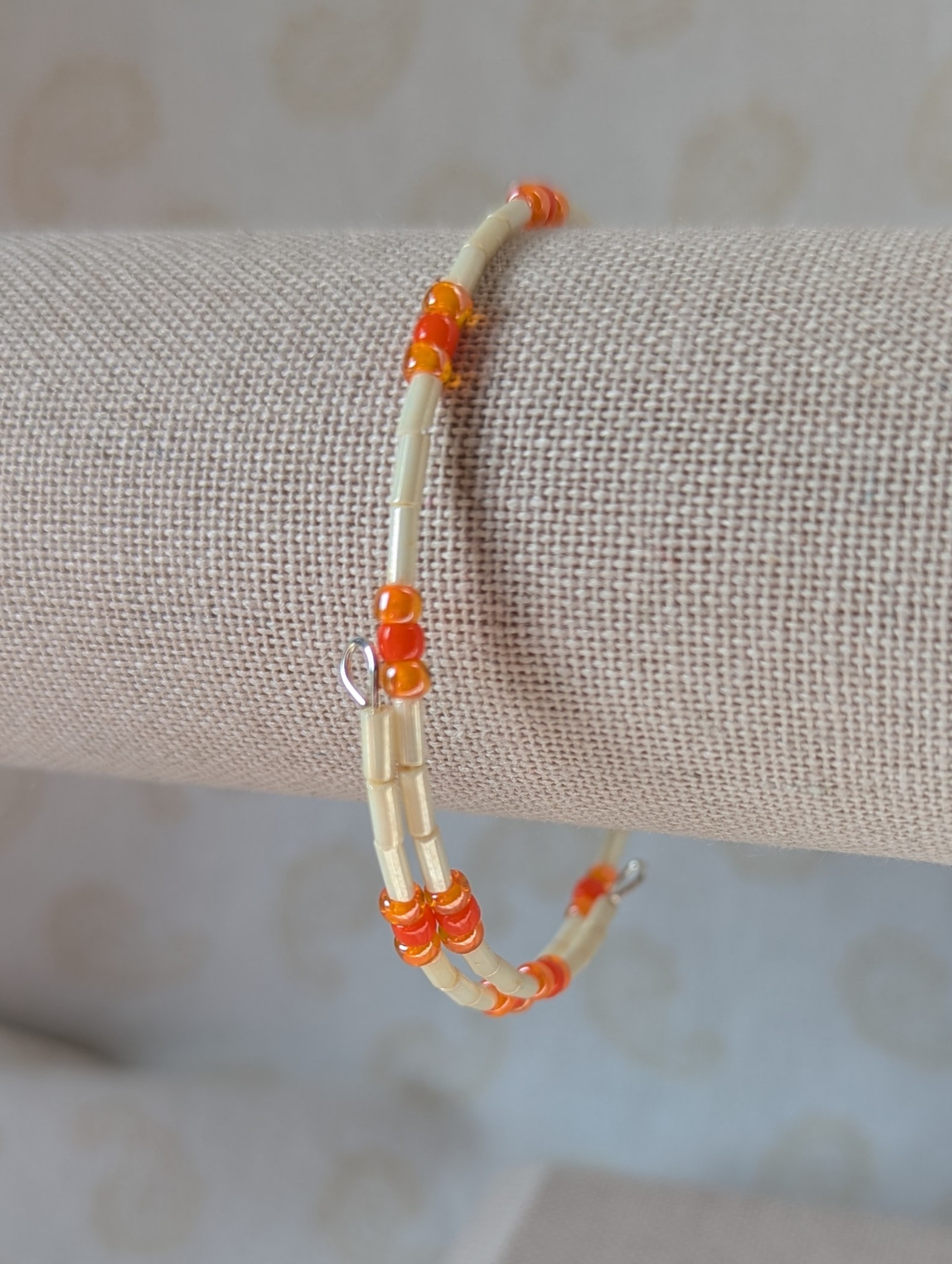 Handmade bracelet with long cream beads, solid orange beads, and orange-lined clear beads arranged in repeating clusters.