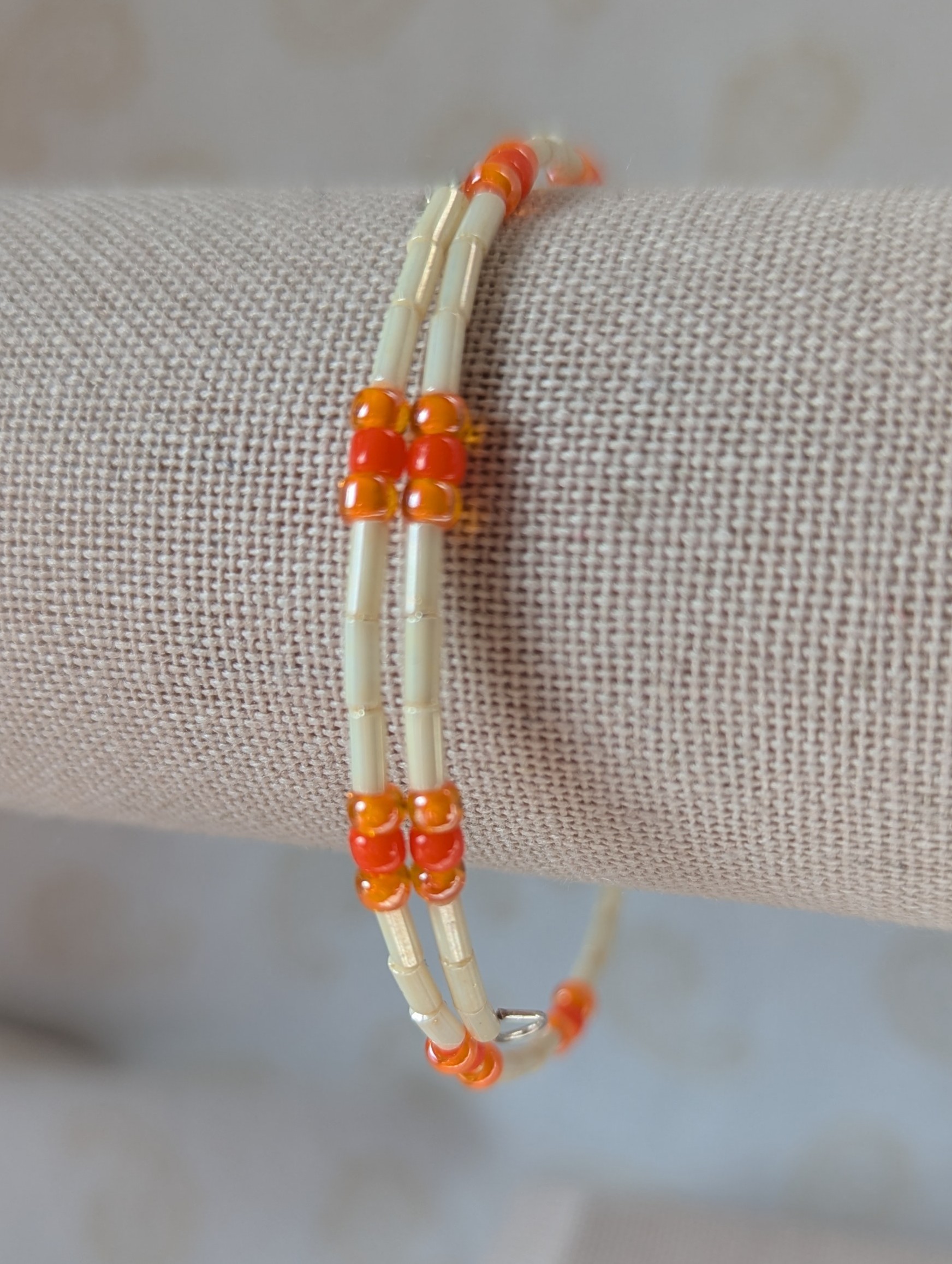 Handmade bracelet with long cream beads, solid orange beads, and orange-lined clear beads arranged in repeating clusters.