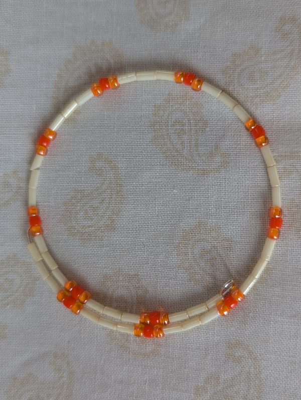 Handmade bracelet with long cream beads, solid orange beads, and orange-lined clear beads arranged in repeating clusters.