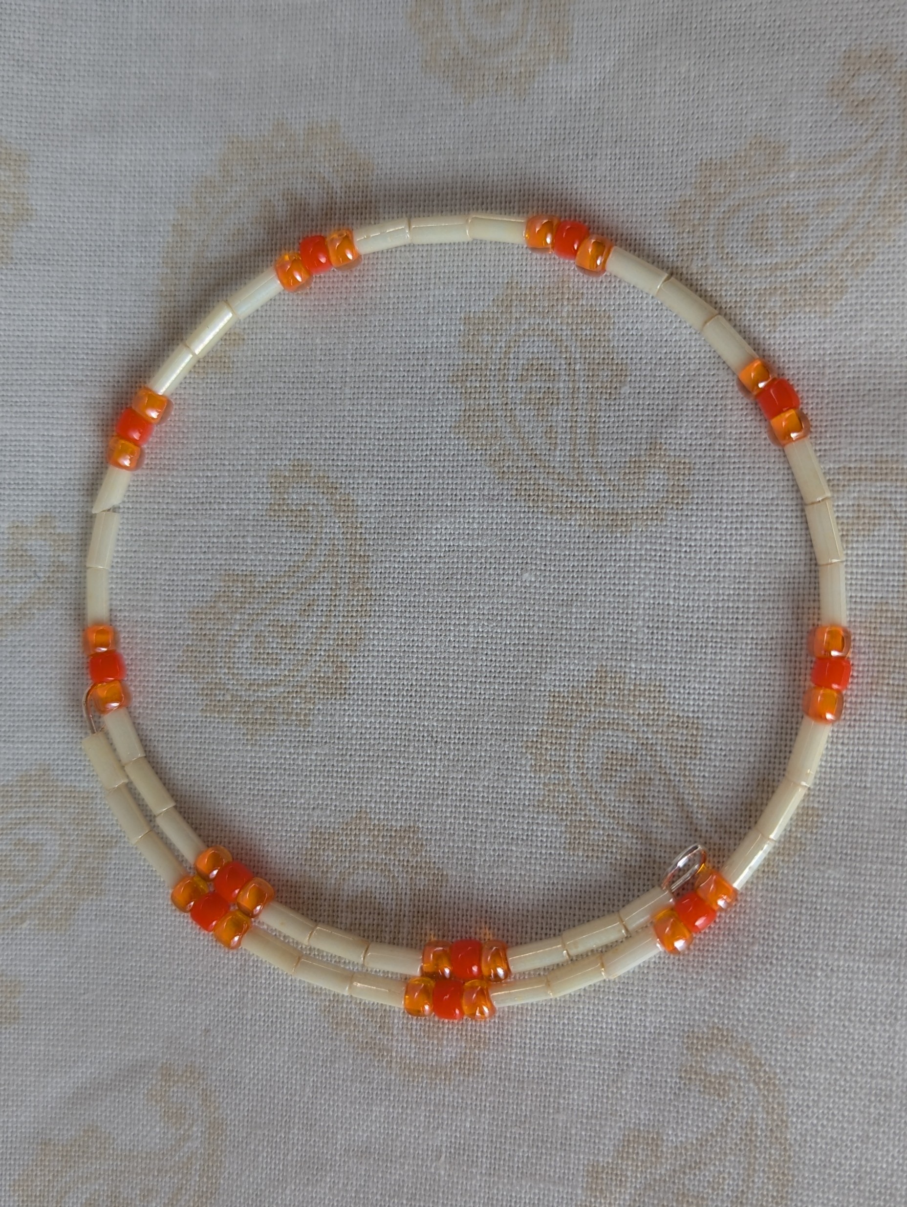 Handmade bracelet with long cream beads, solid orange beads, and orange-lined clear beads arranged in repeating clusters.