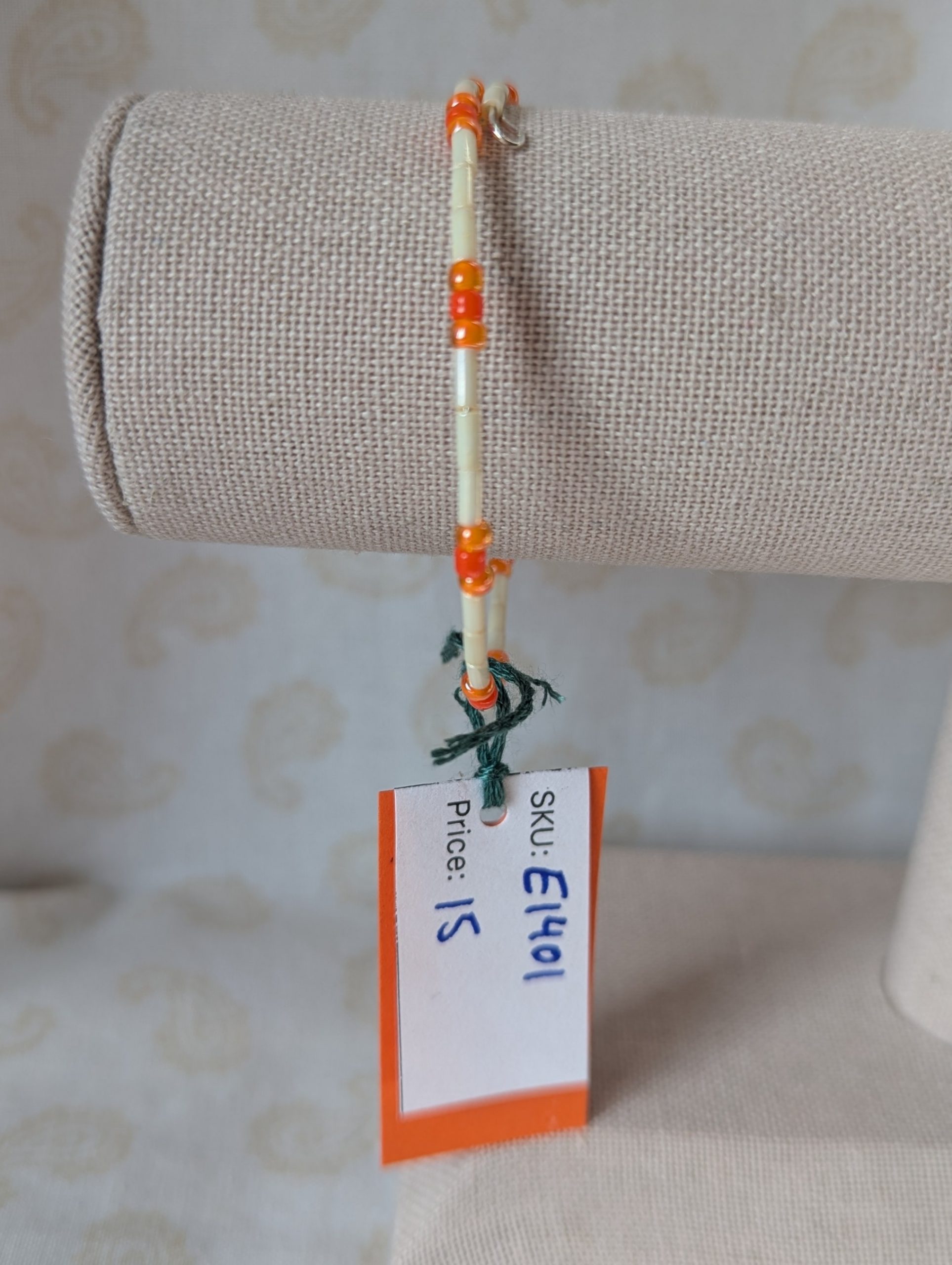 Handmade bracelet with long cream beads, solid orange beads, and orange-lined clear beads arranged in repeating clusters.