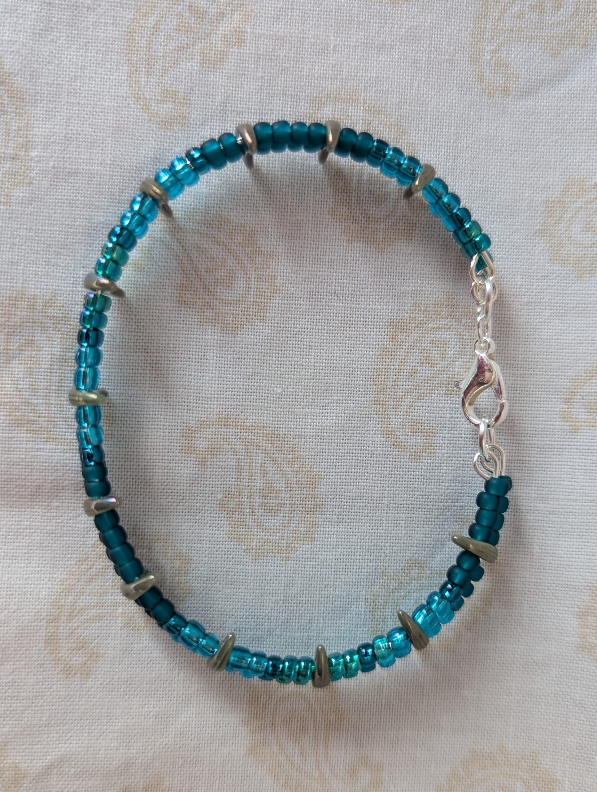Handmade teal crescent bracelet with layered teal seed beads, metallic crescent beads, and a silver lobster clasp.