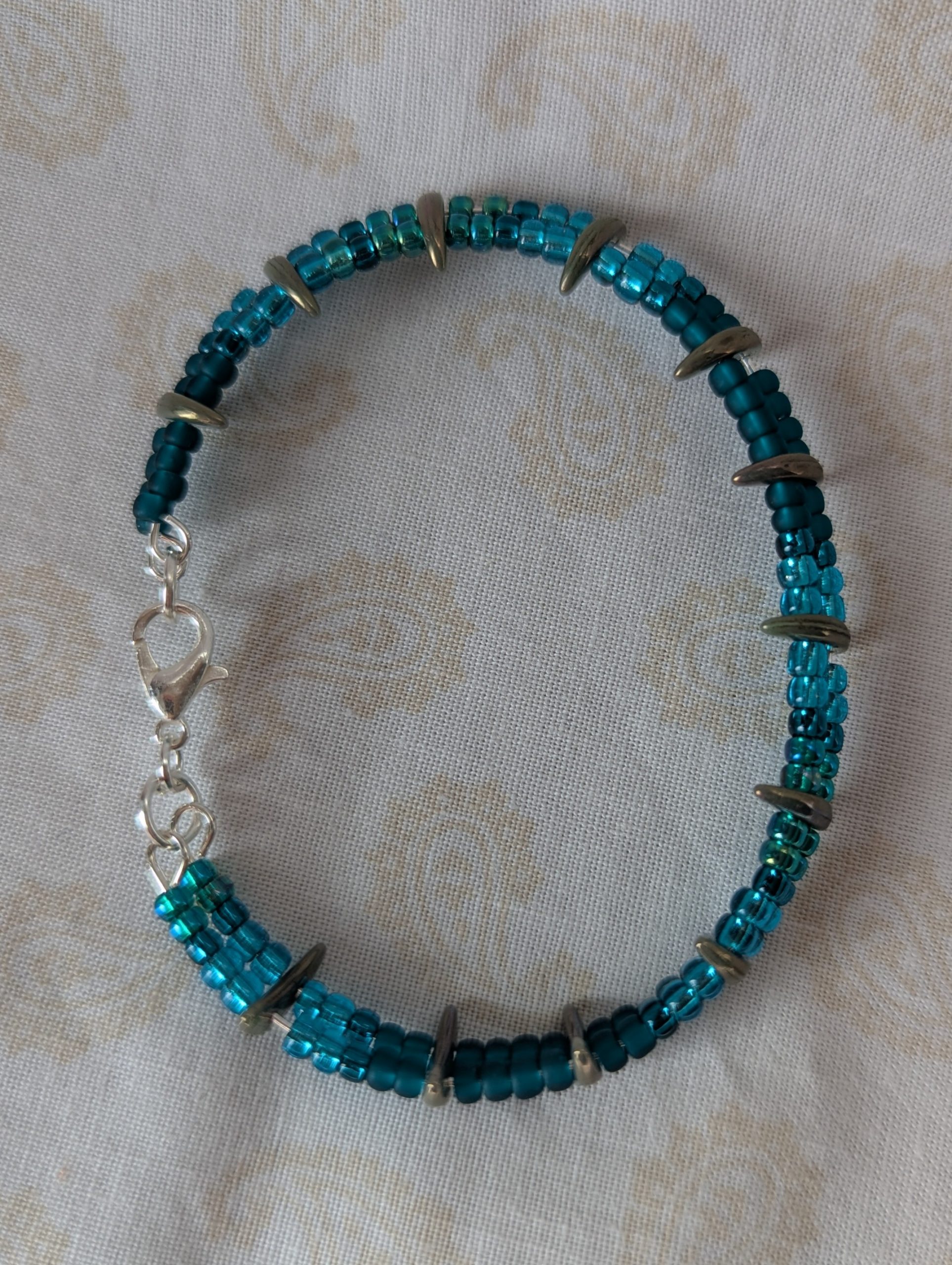 Handmade teal crescent bracelet with layered teal seed beads, metallic crescent beads, and a silver lobster clasp.