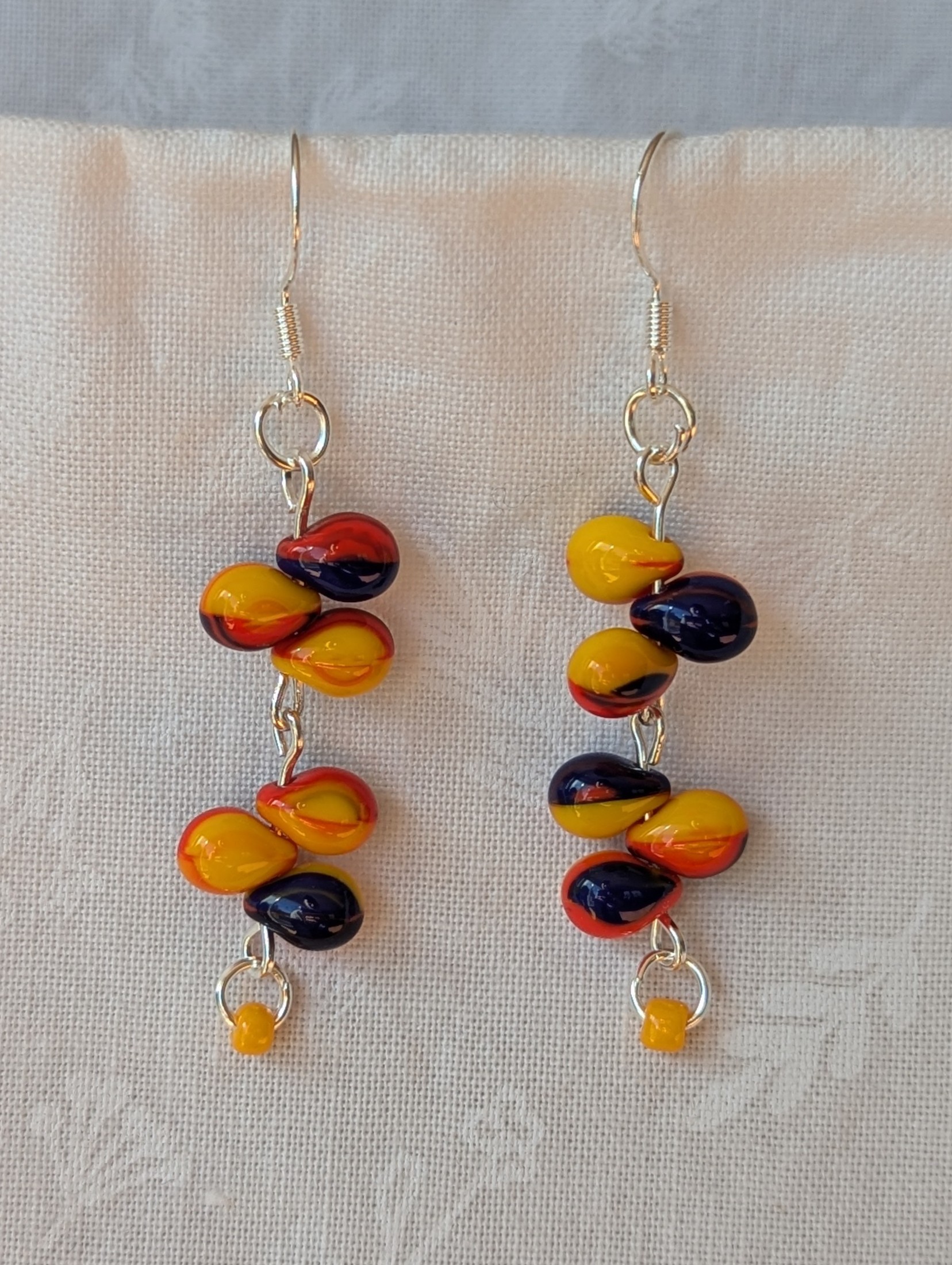 Handmade carnival-themed earrings with cascading yellow, red, and blue glass teardrop beads and a small yellow seed bead on sterling silver hooks.