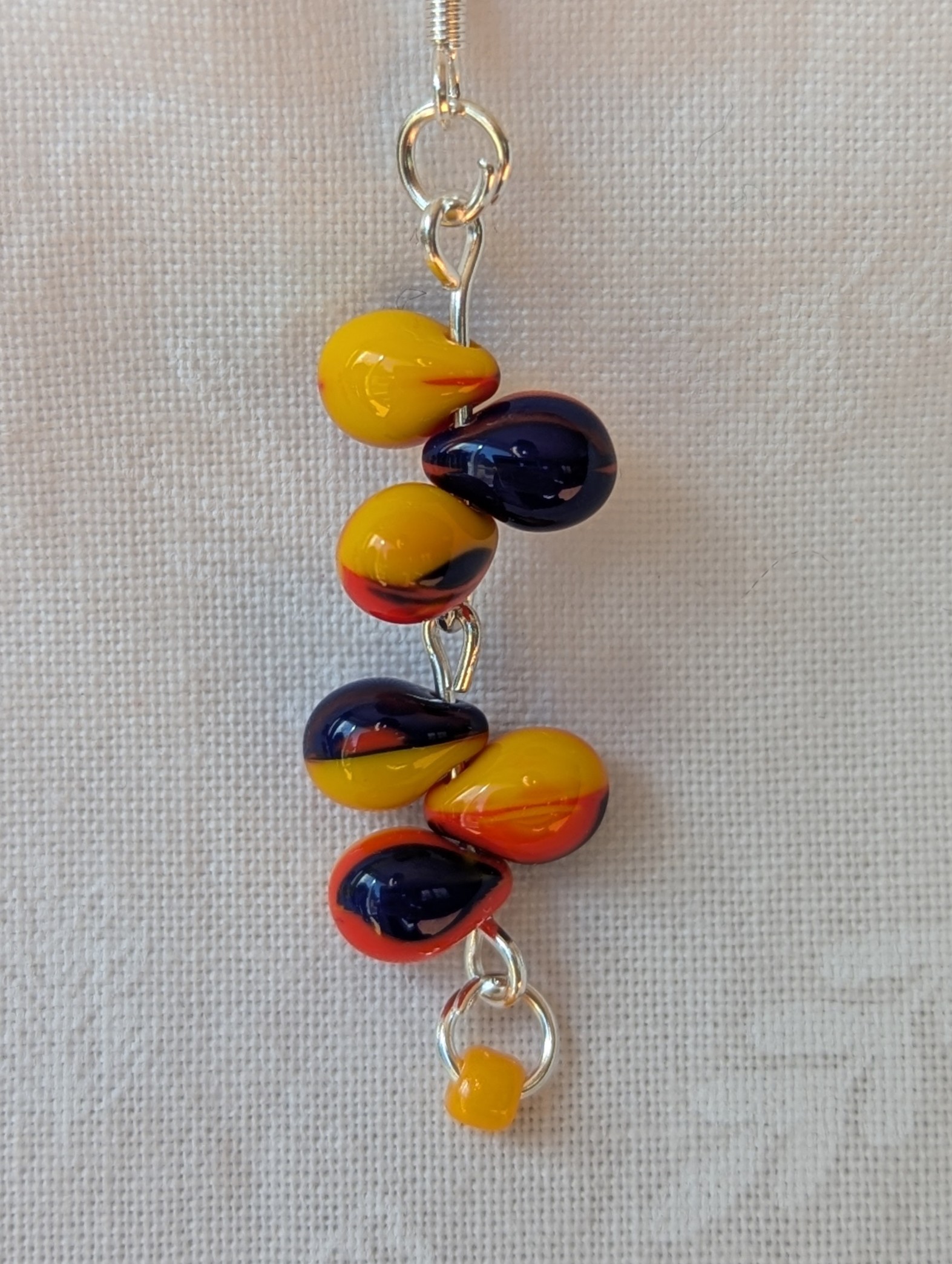 Handmade carnival-themed earrings with cascading yellow, red, and blue glass teardrop beads and a small yellow seed bead on sterling silver hooks.