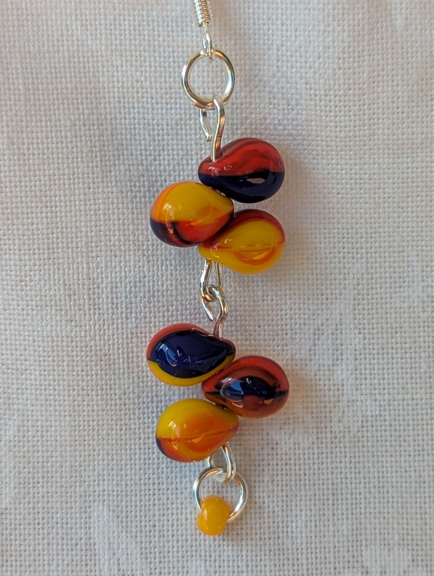 Handmade carnival-themed earrings with cascading yellow, red, and blue glass teardrop beads and a small yellow seed bead on sterling silver hooks.