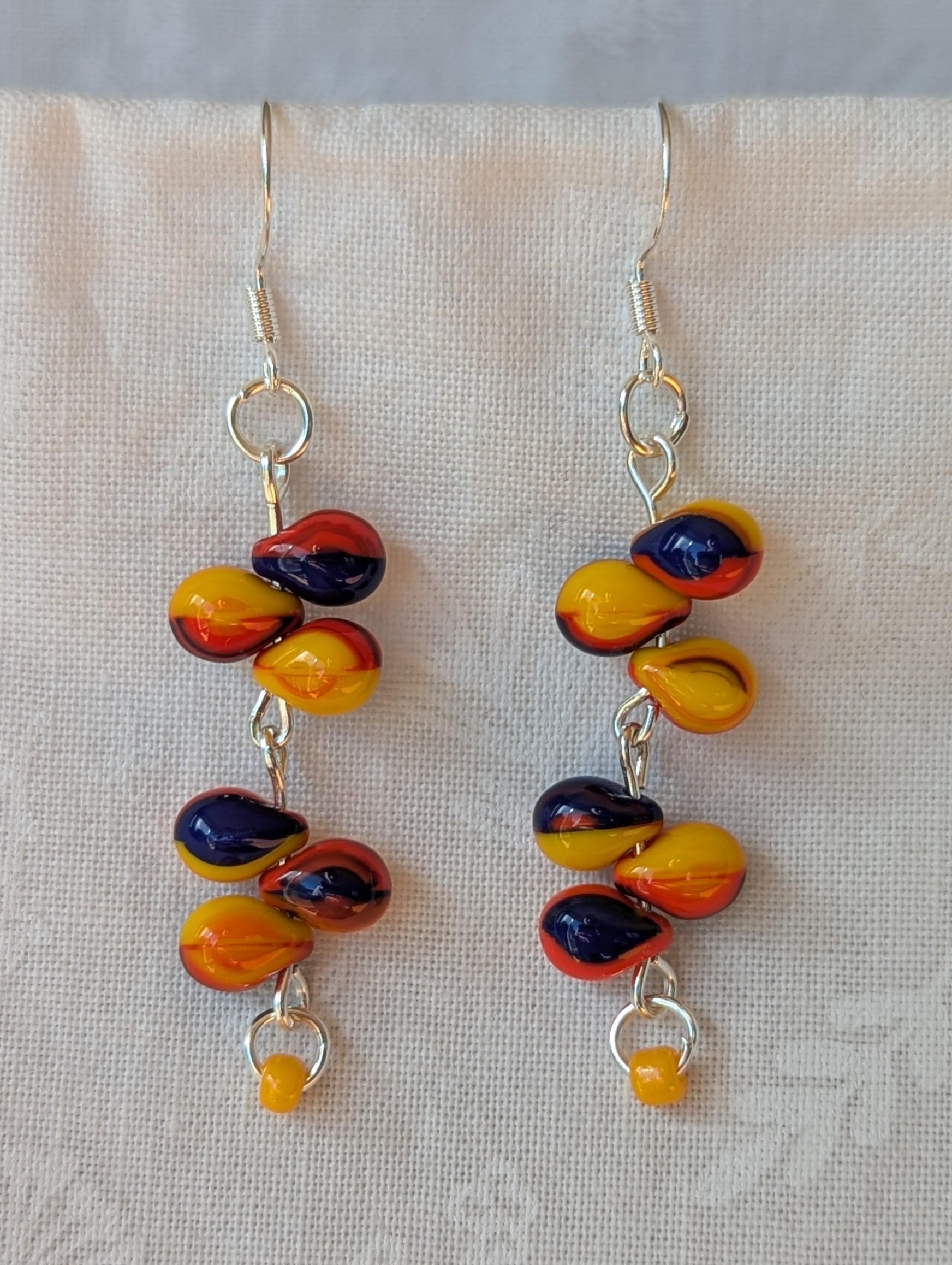 Handmade carnival-themed earrings with cascading yellow, red, and blue glass teardrop beads and a small yellow seed bead on sterling silver hooks.