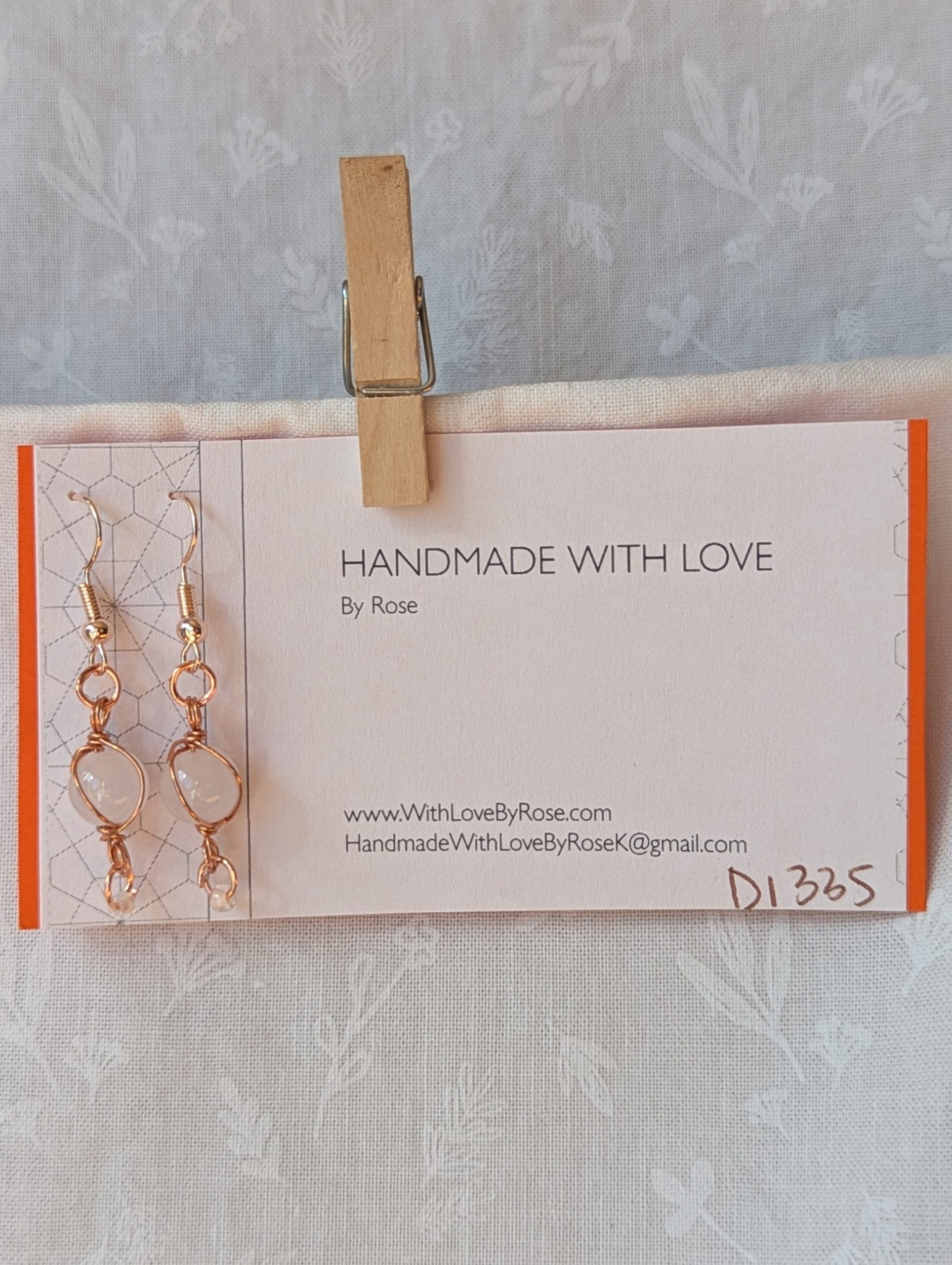 Handmade earrings featuring a milky white glass bead wrapped in copper wire with a white seed bead dangling below, hung from rose-gold colored hooks — Moonlit Copper Glow Earrings.