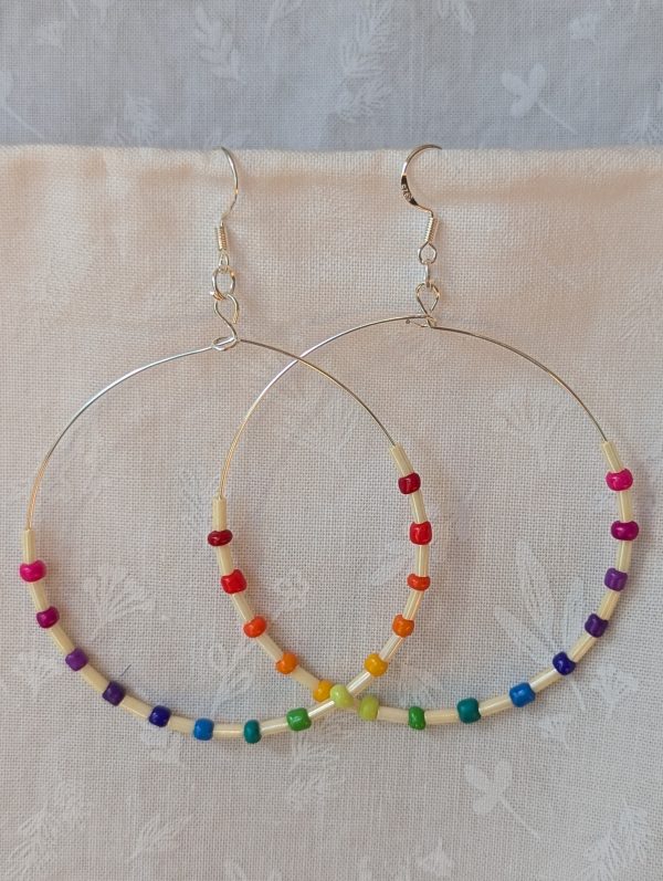 Handmade rainbow and cream accent hoop earrings with alternating colorful glass seed beads and long cream beads on silver-plated wire with sterling silver hooks.