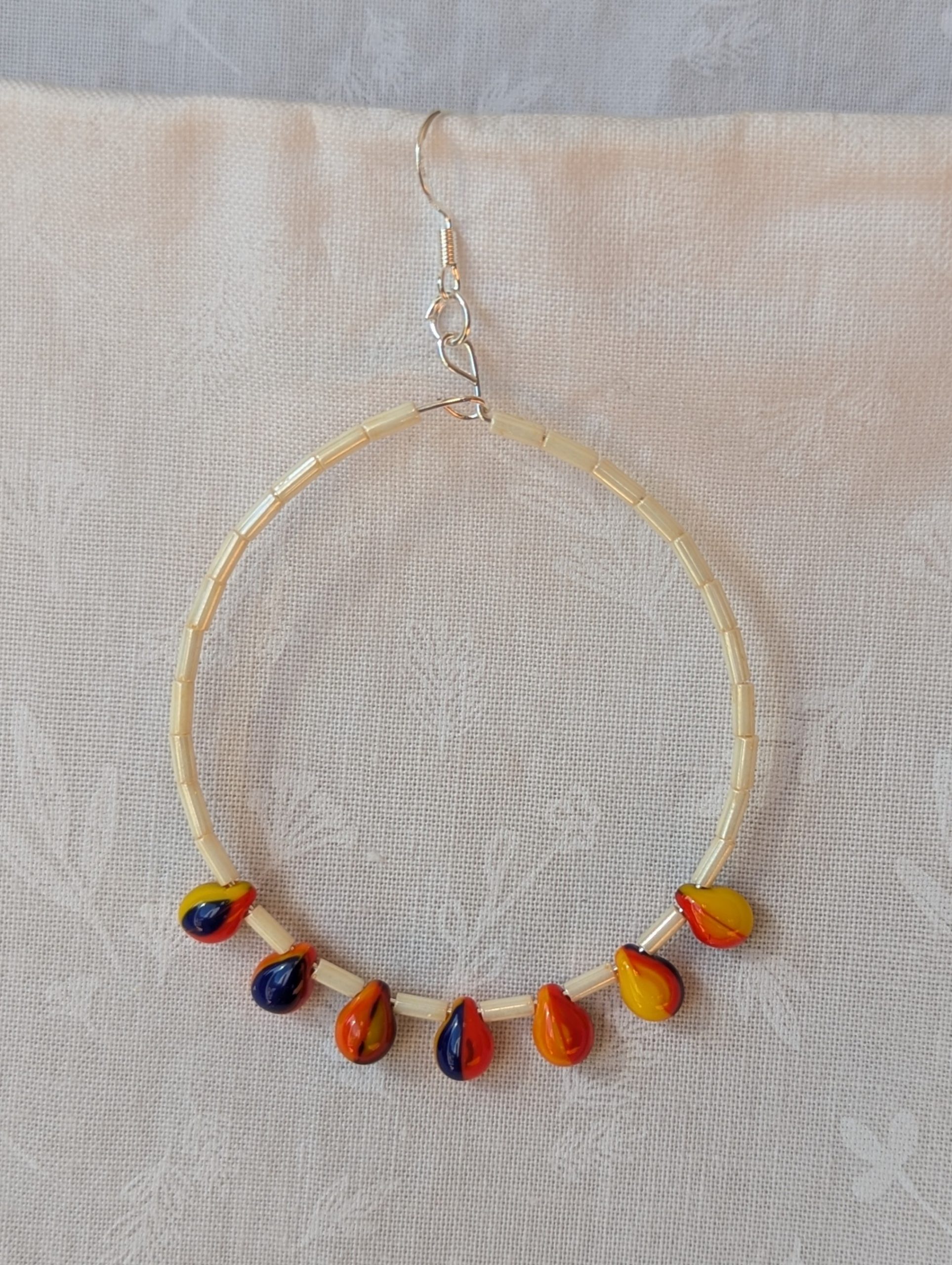 Large cream beaded hoop earrings with multicolor glass teardrop beads in red, yellow, and navy blue on silver-plated wire with sterling silver hooks.