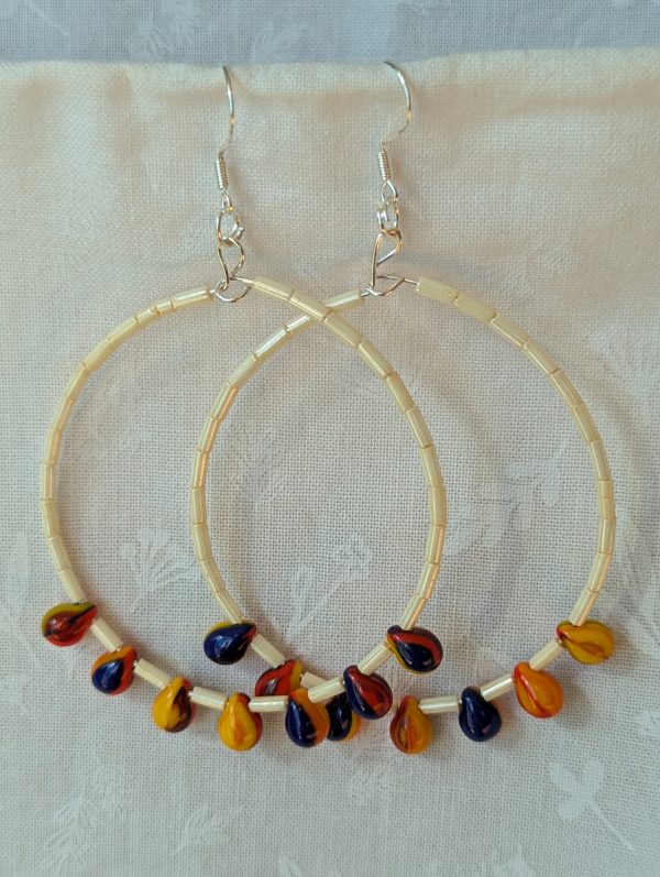 Large cream beaded hoop earrings with multicolor glass teardrop beads in red, yellow, and navy blue on silver-plated wire with sterling silver hooks.