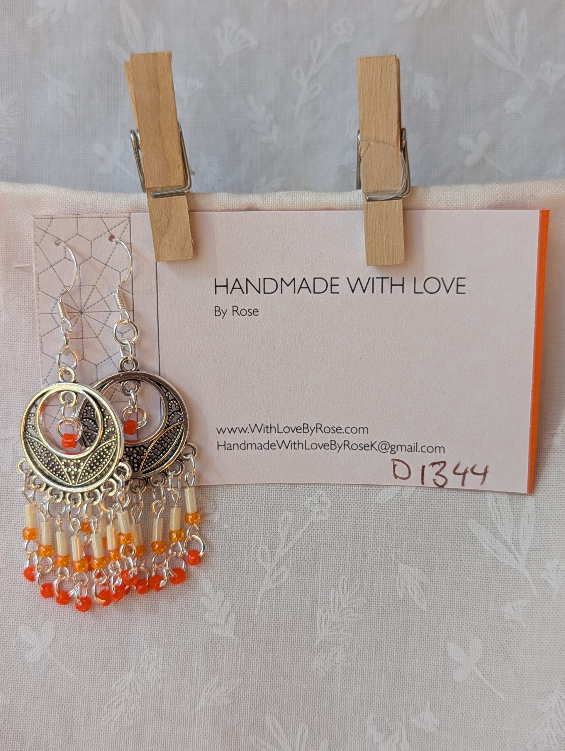 Orange and silver beaded decorative dangle earrings with cream, pale orange, and dark orange glass beads hanging in cascading strands from a silver ornamental medallion.