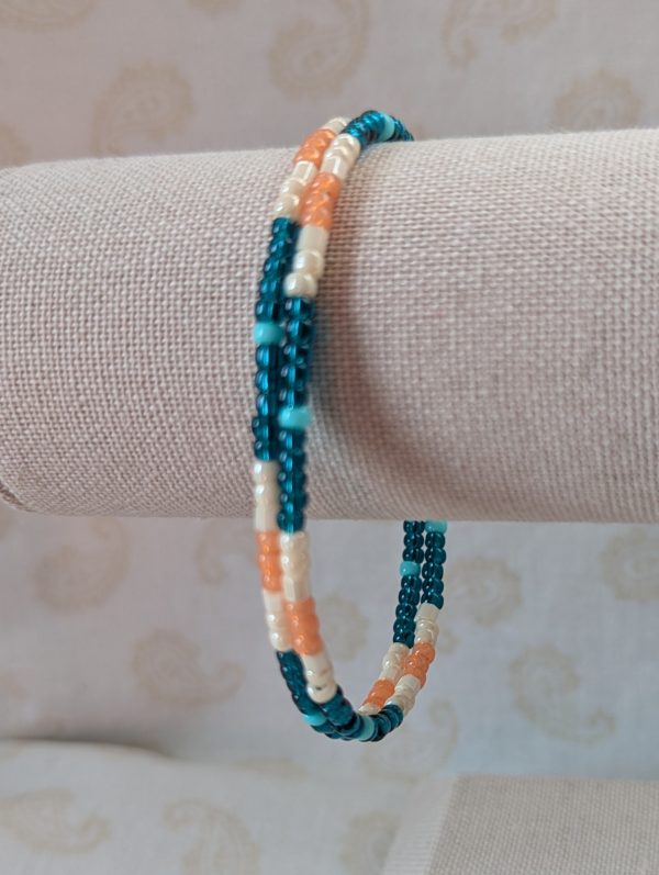 Handmade teal and cream bracelet with salmon and pale teal beads on stretch wire with overlap closure.