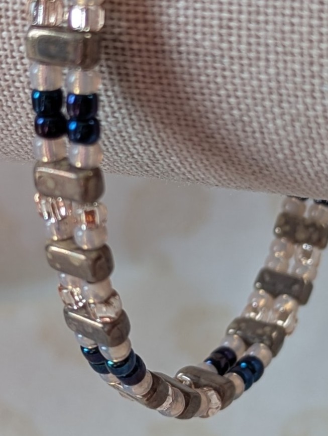 Double-strand memory wire bracelet with pale pink, iridescent blue seed beads and taupe rectangular stone beads, finished with a silver lobster clasp.