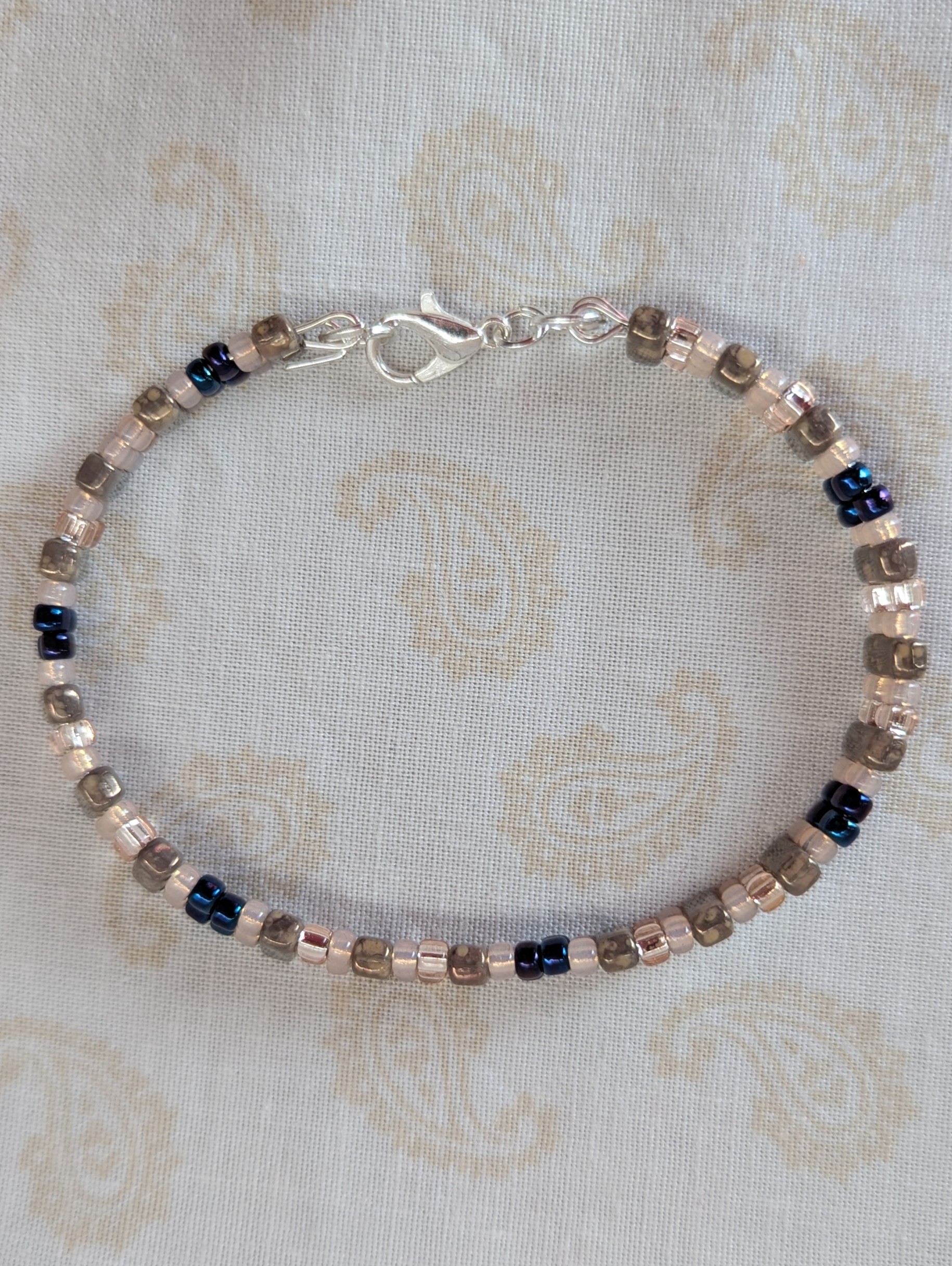Double-strand memory wire bracelet with pale pink, iridescent blue seed beads and taupe rectangular stone beads, finished with a silver lobster clasp.