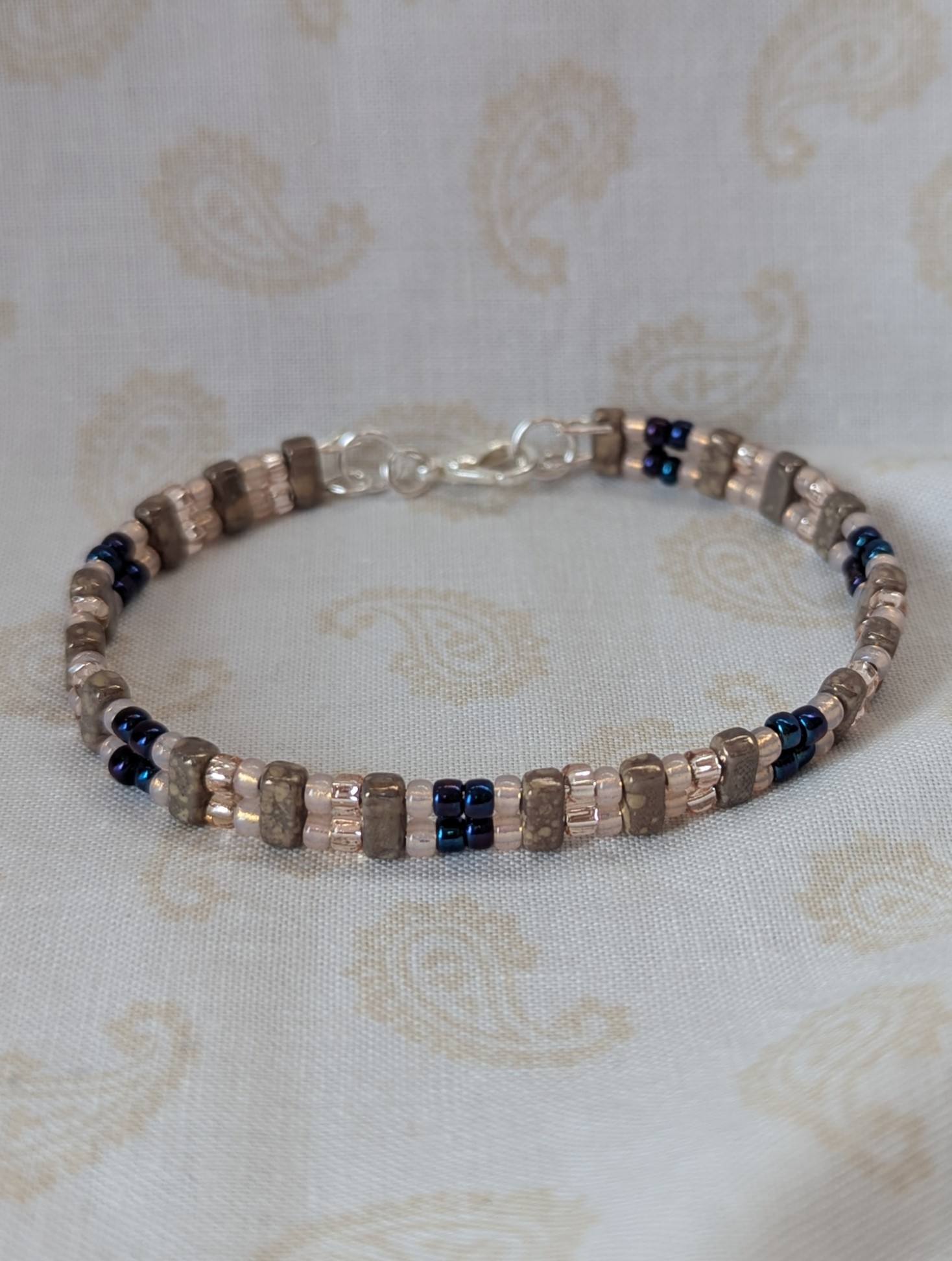 Double-strand memory wire bracelet with pale pink, iridescent blue seed beads and taupe rectangular stone beads, finished with a silver lobster clasp.