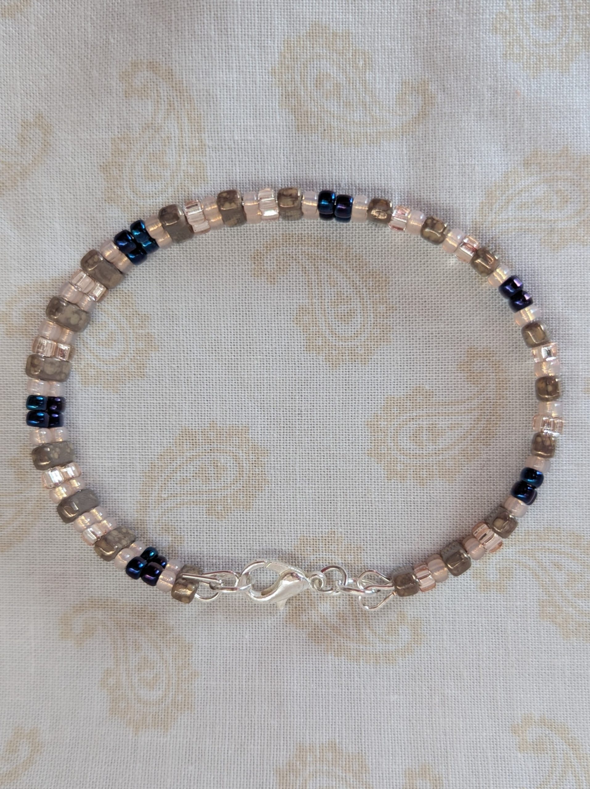 Double-strand memory wire bracelet with pale pink, iridescent blue seed beads and taupe rectangular stone beads, finished with a silver lobster clasp.