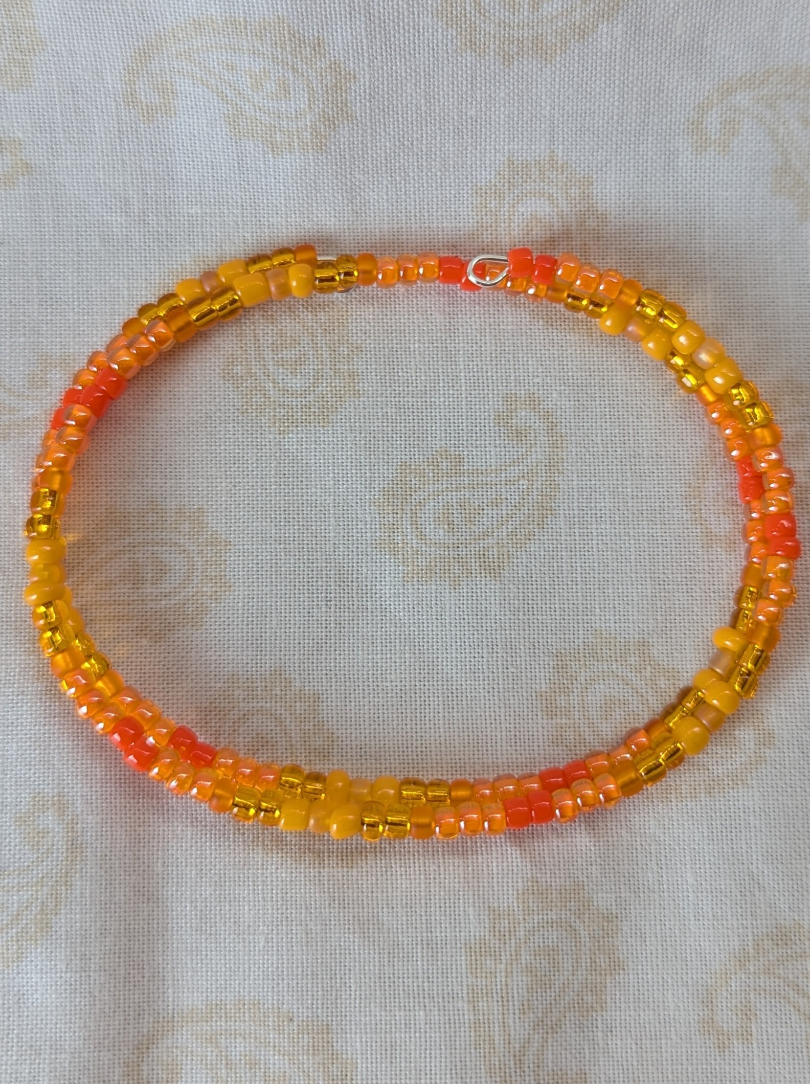 Orange memory wire bracelet with multiple shades and textures of orange glass beads, stretchy design with no clasp.
