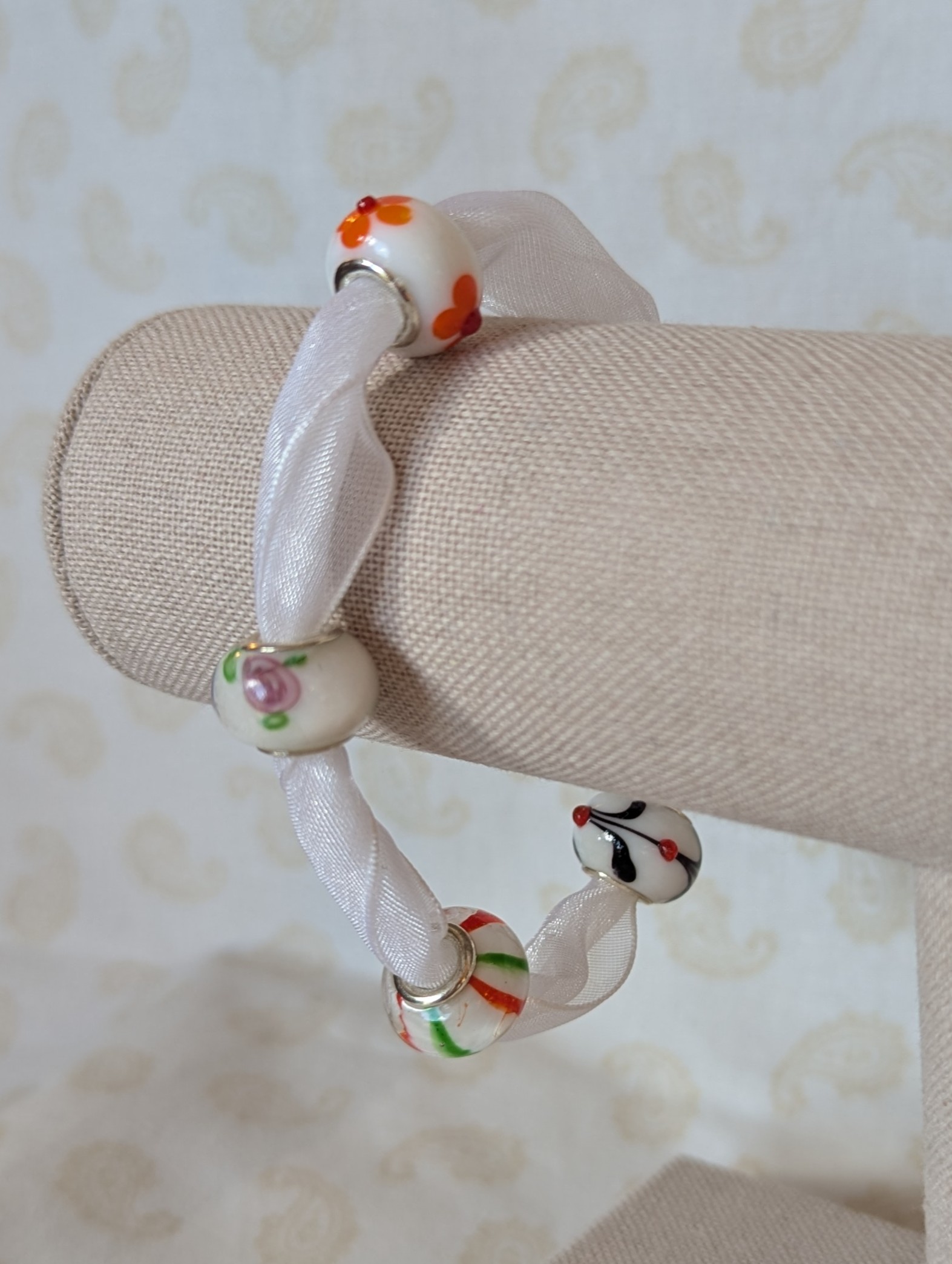 Petal Drift White Lampwork Ribbon Bracelet with sheer white ribbon, four decorative glass beads with colorful floral and stripe details, and lobster clasp
