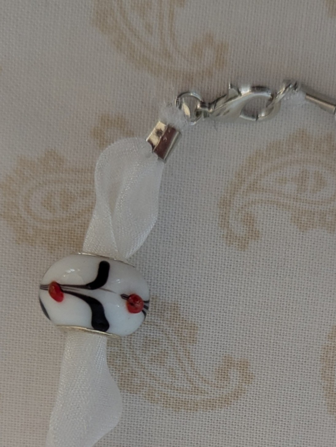 Petal Drift White Lampwork Ribbon Bracelet with sheer white ribbon, four decorative glass beads with colorful floral and stripe details, and lobster clasp