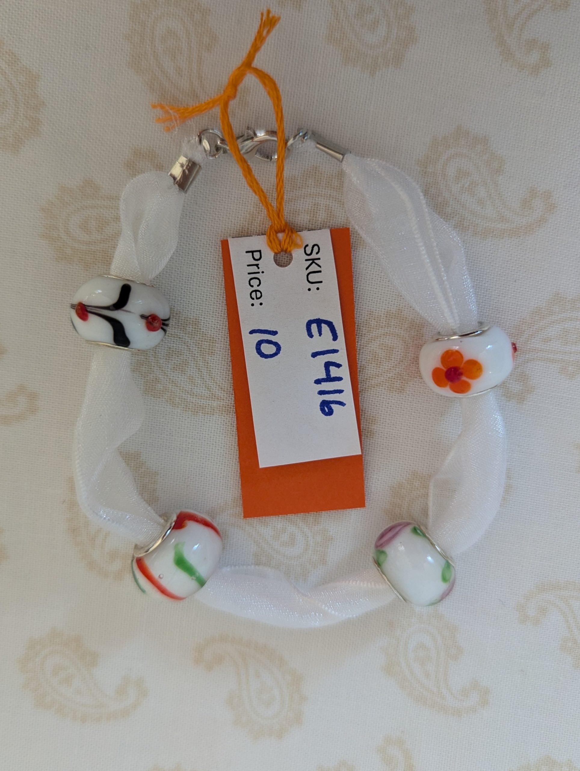 Petal Drift White Lampwork Ribbon Bracelet with sheer white ribbon, four decorative glass beads with colorful floral and stripe details, and lobster clasp