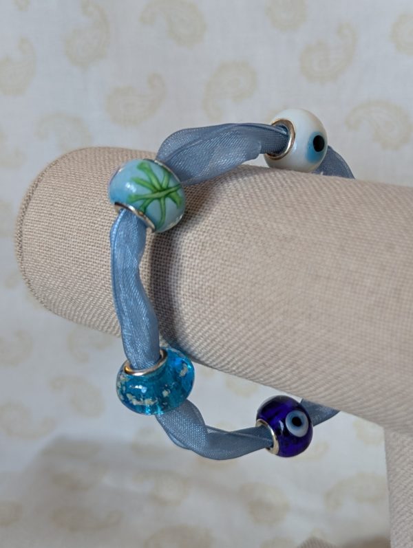 Skybound Blue Whisper Ribbon Bracelet with pale blue ribbon, four blue and white decorative glass lampwork-style beads, and silver lobster clasp closure