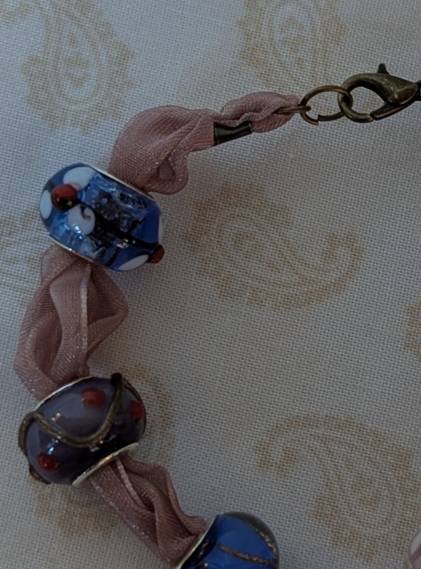 Purple ribbon bracelet with five lampwork-style beads in blue, purple, and pink tones, finished with a lobster clasp.