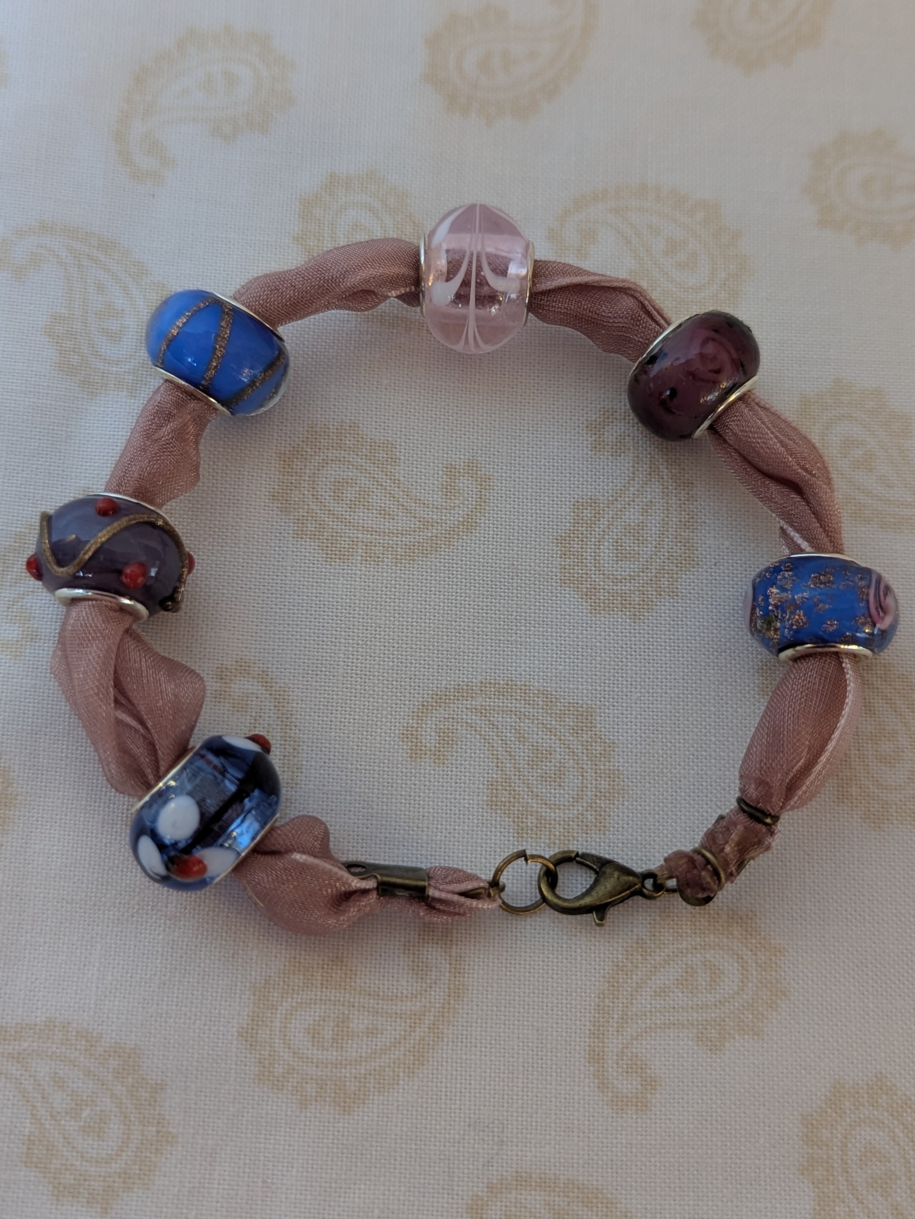 Purple ribbon bracelet with five lampwork-style beads in blue, purple, and pink tones, finished with a lobster clasp.