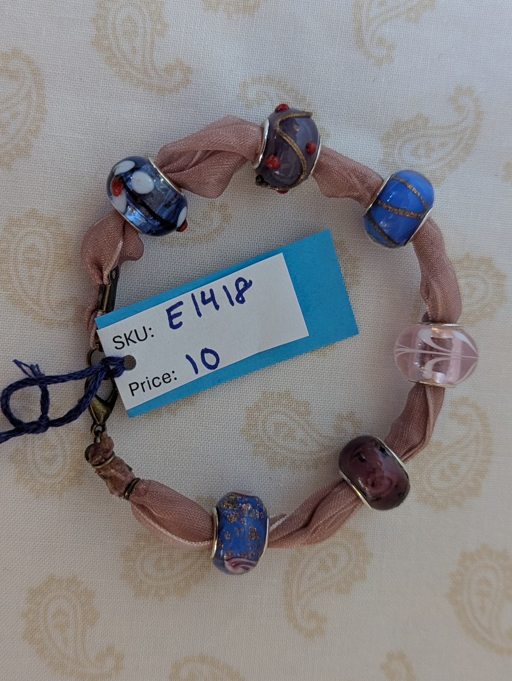 Purple ribbon bracelet with five lampwork-style beads in blue, purple, and pink tones, finished with a lobster clasp.