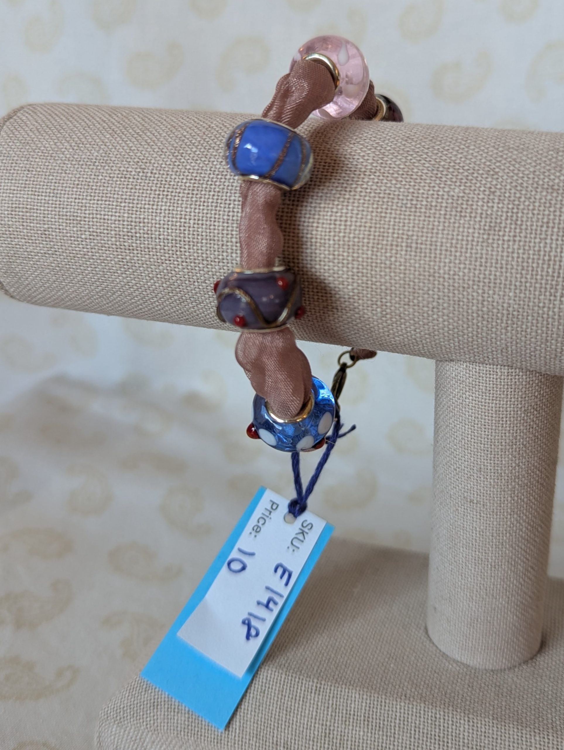 Purple ribbon bracelet with five lampwork-style beads in blue, purple, and pink tones, finished with a lobster clasp.