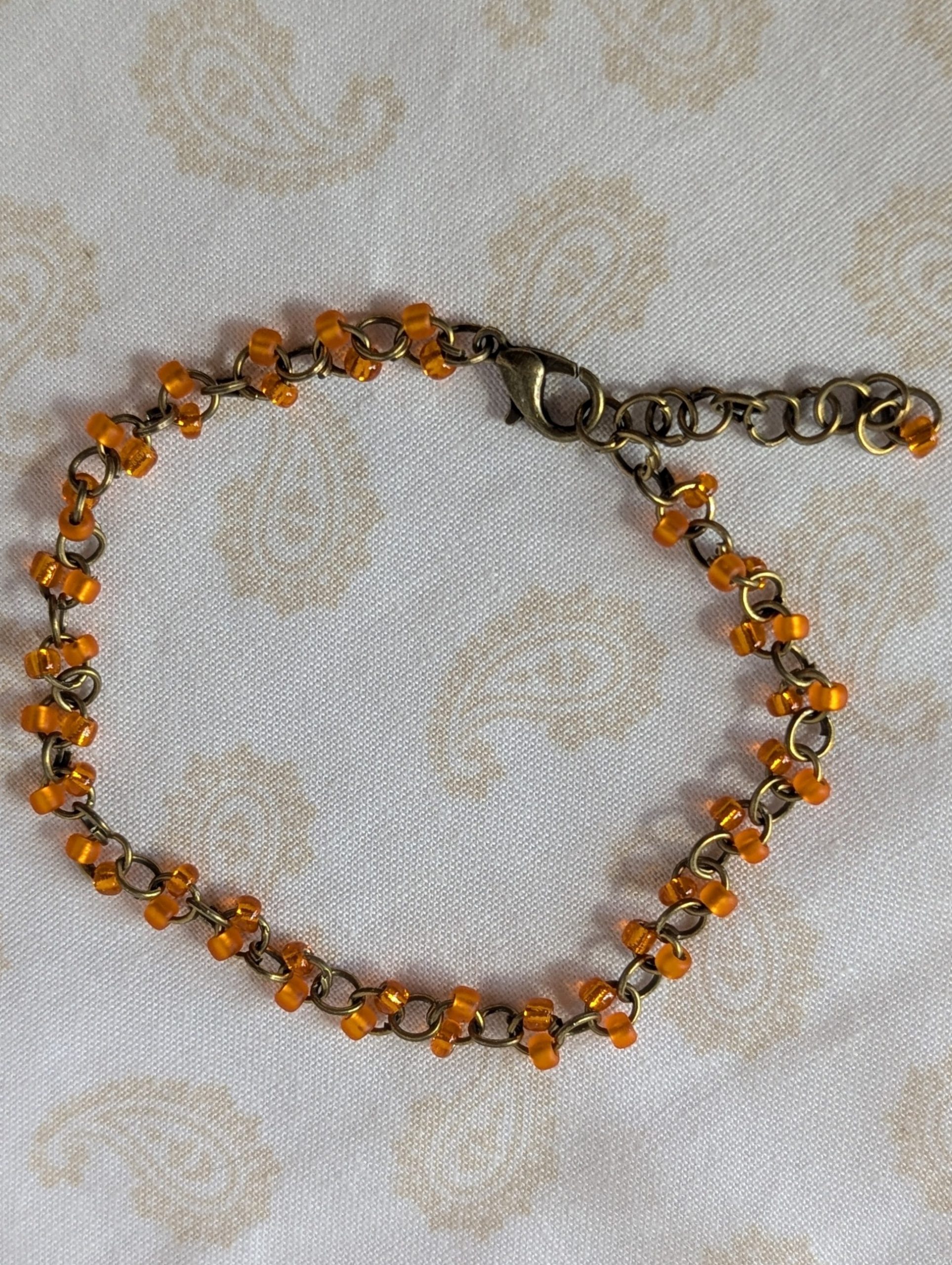 Orange seed bead bracelet with hand-linked bronze chain, matte and silver-lined orange beads, and bronze lobster clasp