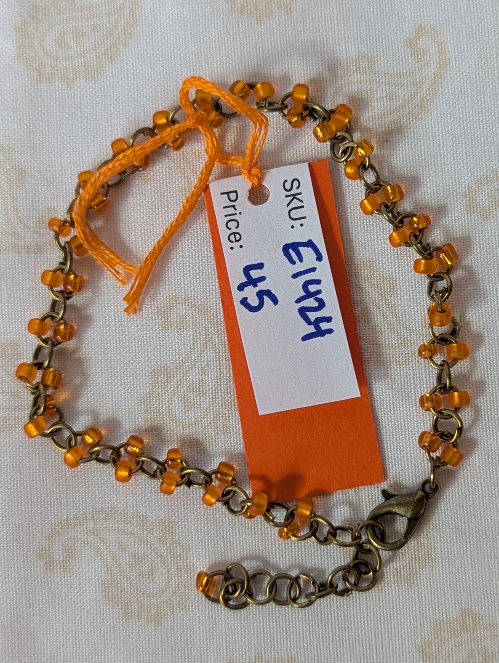 Orange seed bead bracelet with hand-linked bronze chain, matte and silver-lined orange beads, and bronze lobster clasp