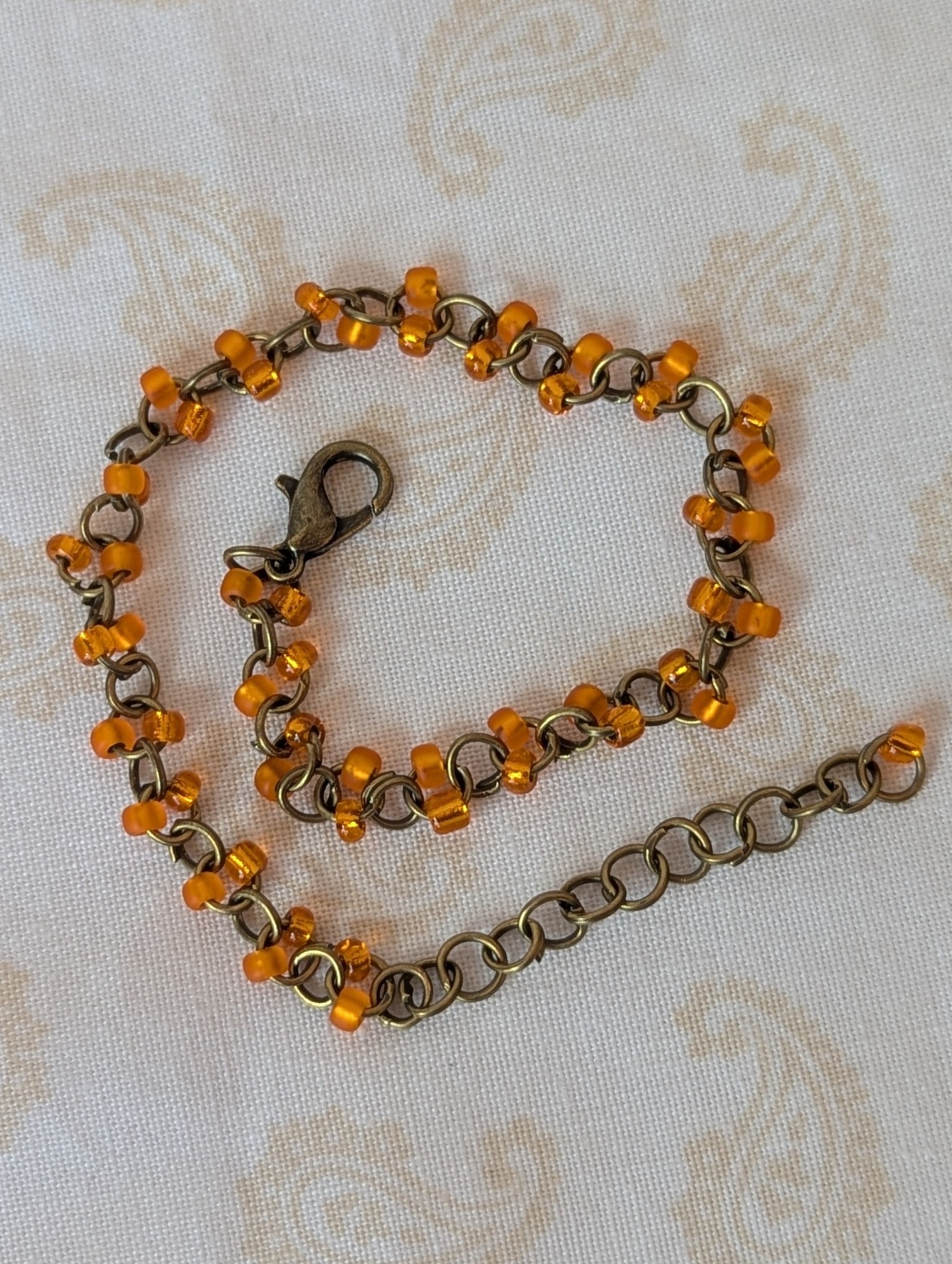Orange seed bead bracelet with hand-linked bronze chain, matte and silver-lined orange beads, and bronze lobster clasp