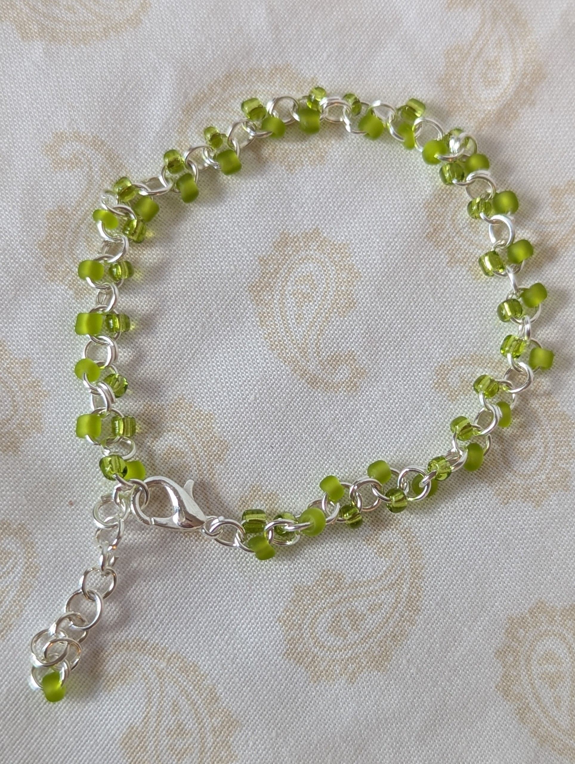 Silver-colored, hand-linked chain bracelet with paired green seed beads, featuring matte lime green and silver-lined lettuce green glass beads and a lobster clasp.