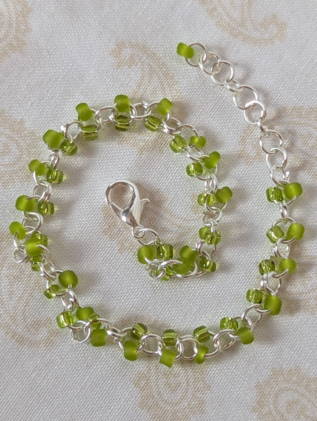 Silver-colored, hand-linked chain bracelet with paired green seed beads, featuring matte lime green and silver-lined lettuce green glass beads and a lobster clasp.
